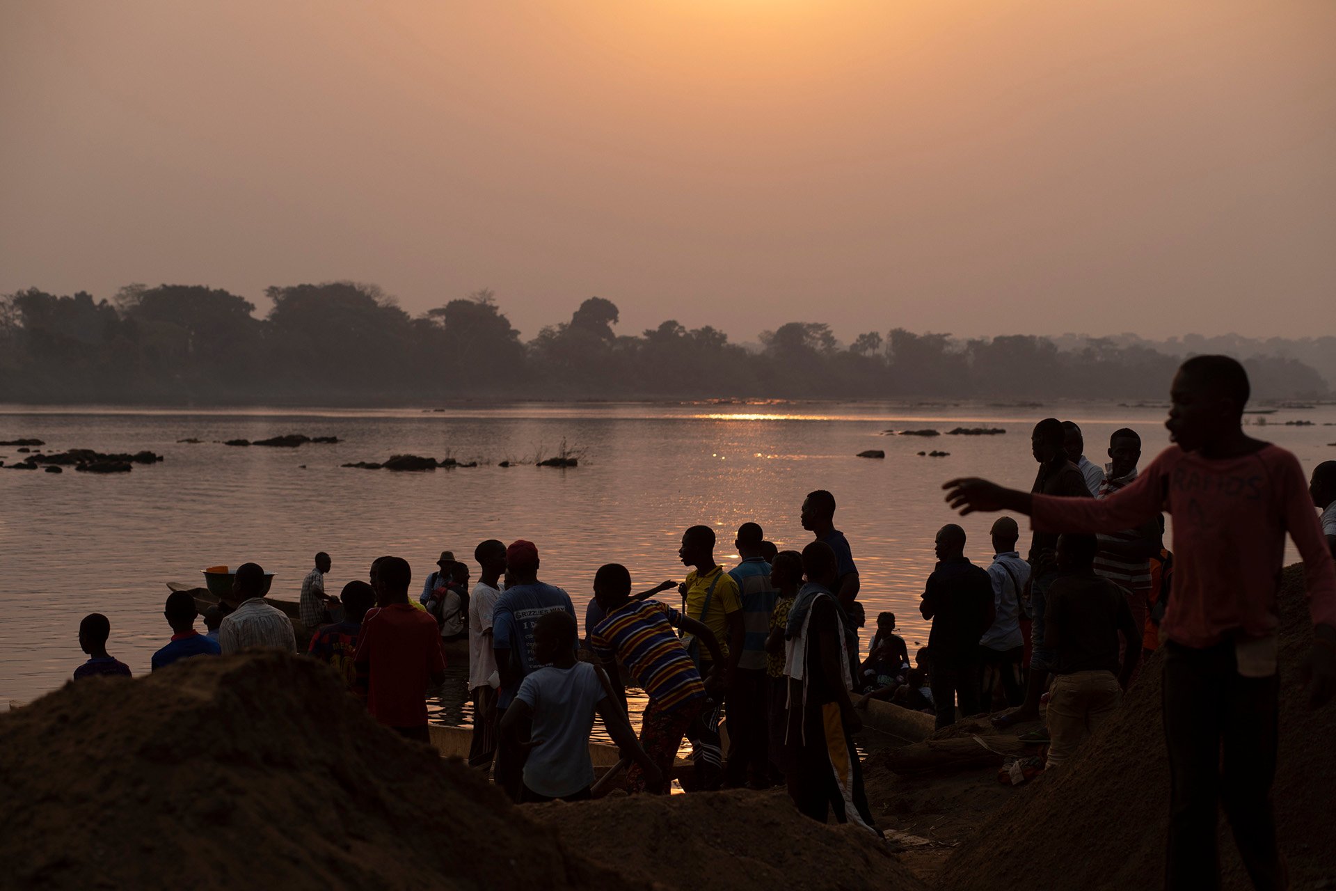 People stand on a riverbank in dim lighting. 