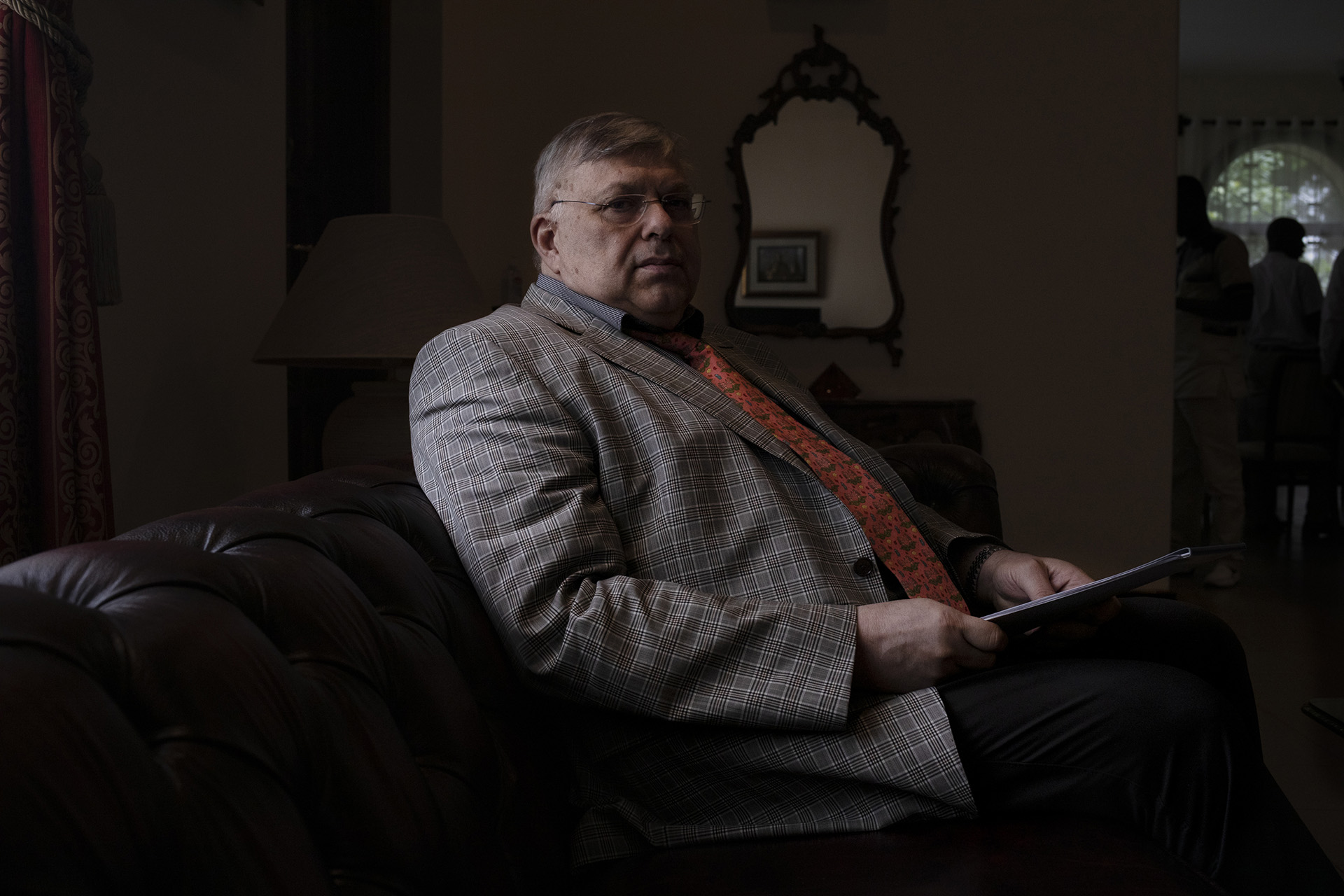 A man sits in a chair behind a desk in a dark room.