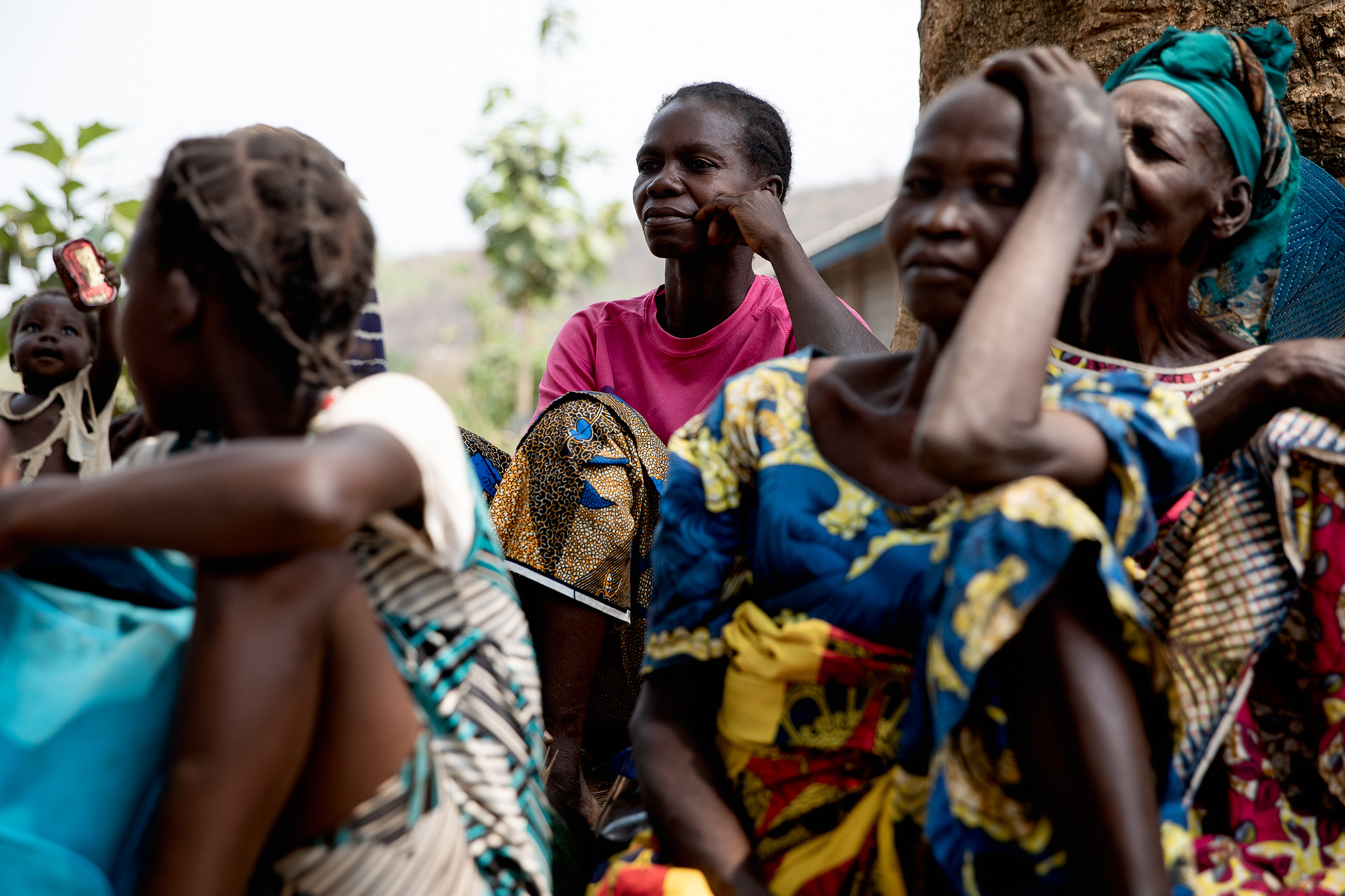 A woman in a pink t-shirt at the centre of the image is in focus, looking past the camera to the left. In the foreground are blurry images of other women.