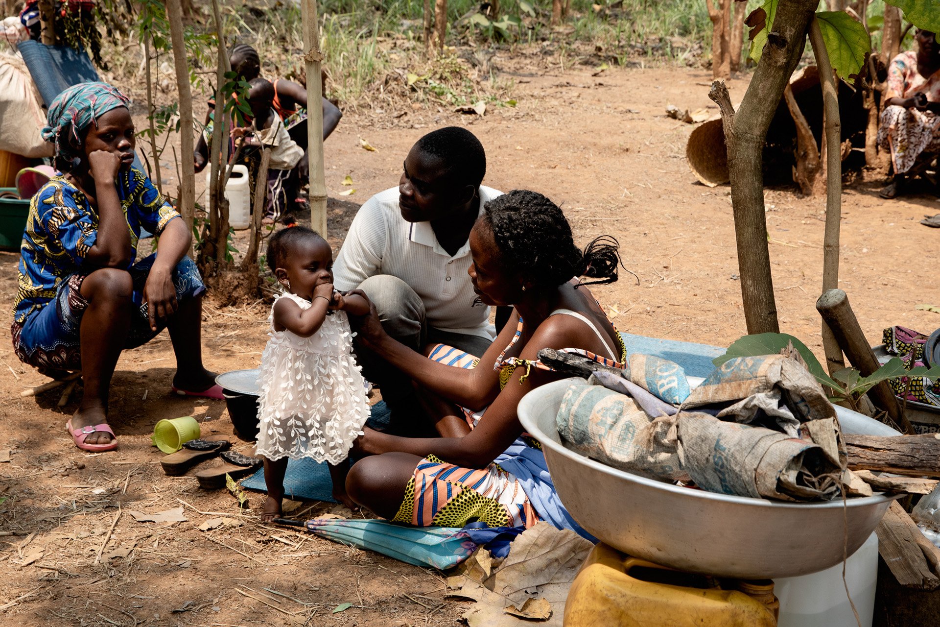 A woman sitting on the ground on a blanket plays with her child who is dressed in white. 