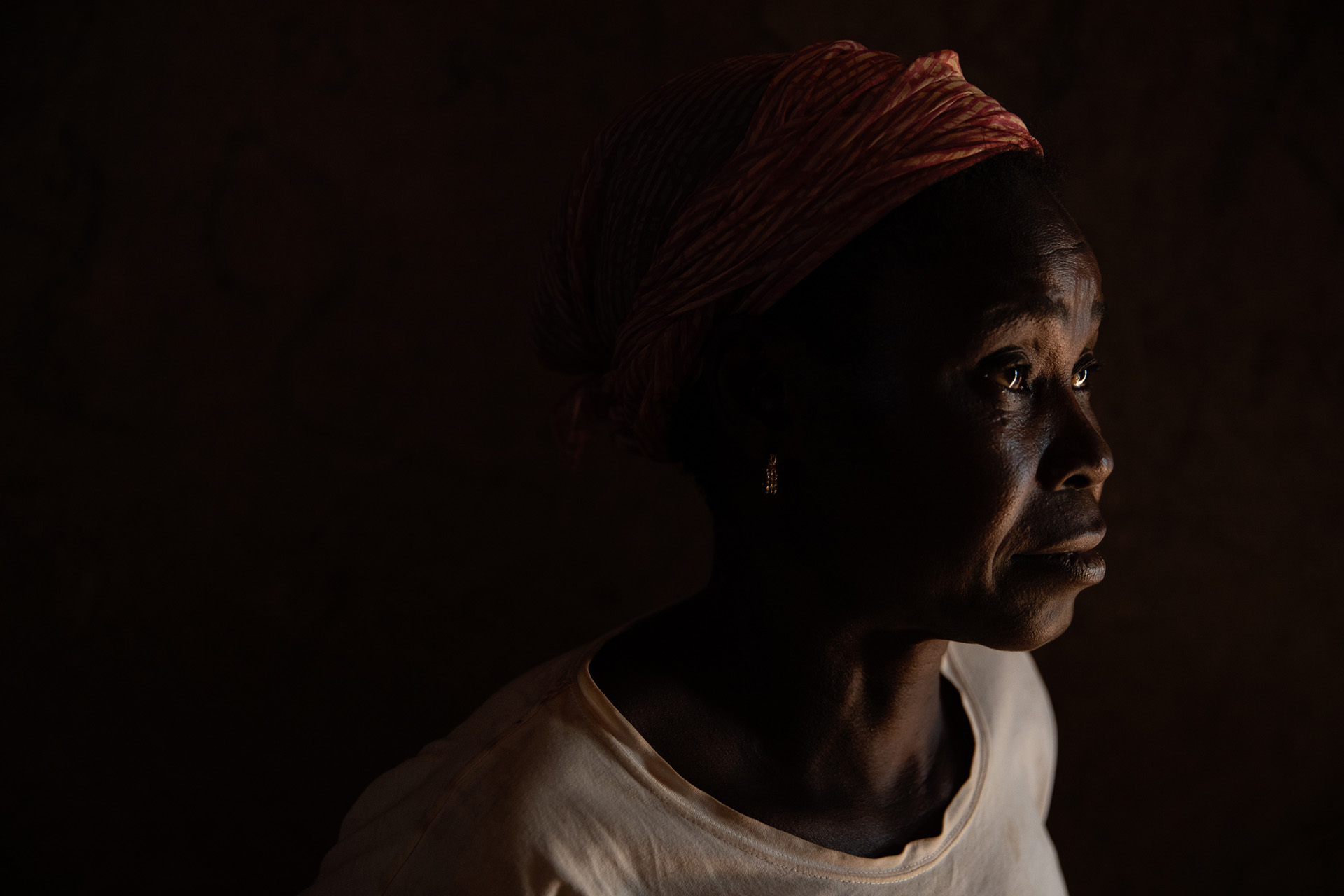 The profile of a woman who looks past the camera to the right, her face softly lit. The rest of the image is dark. 