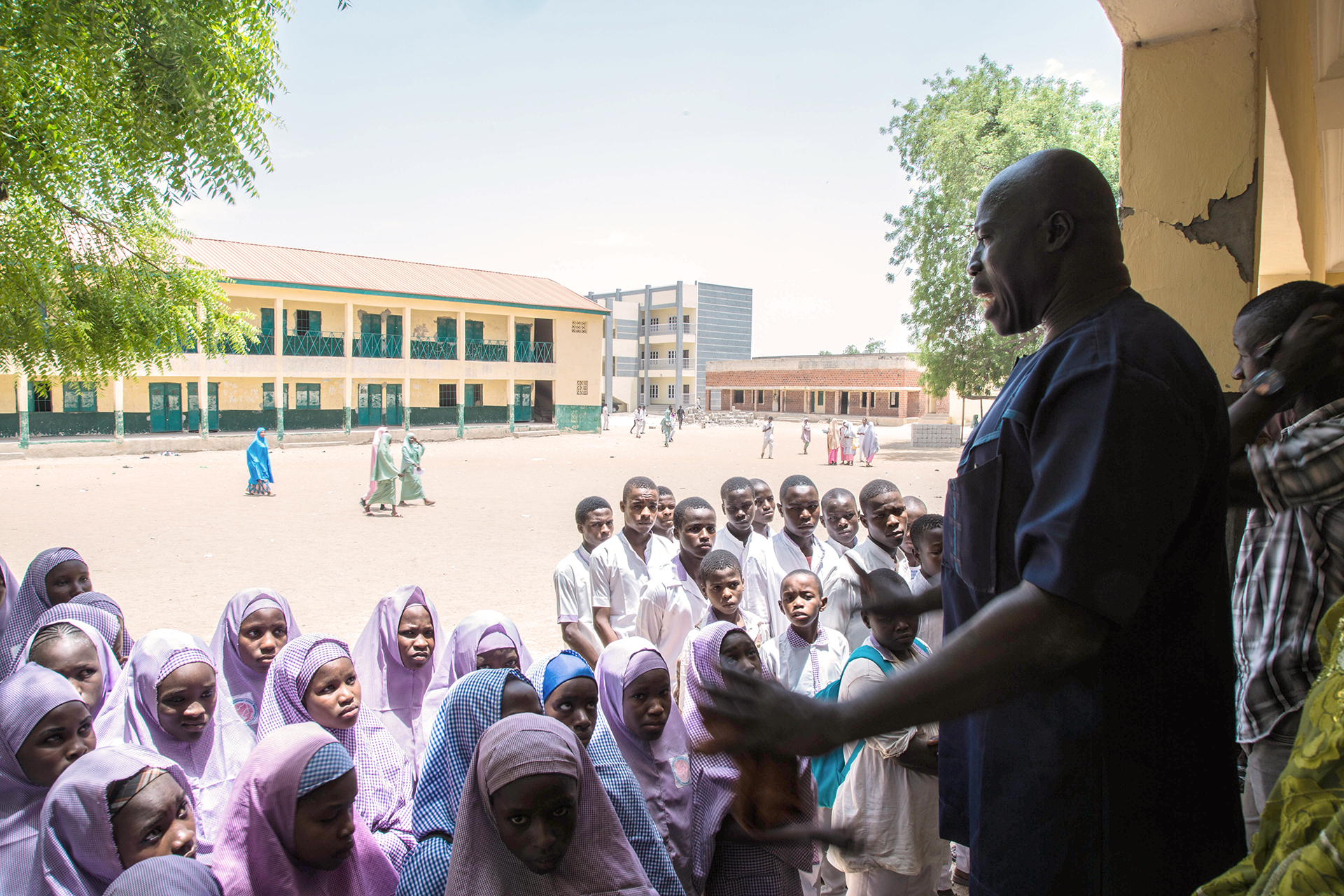 A man stands talking to a group of boys and girls at a school