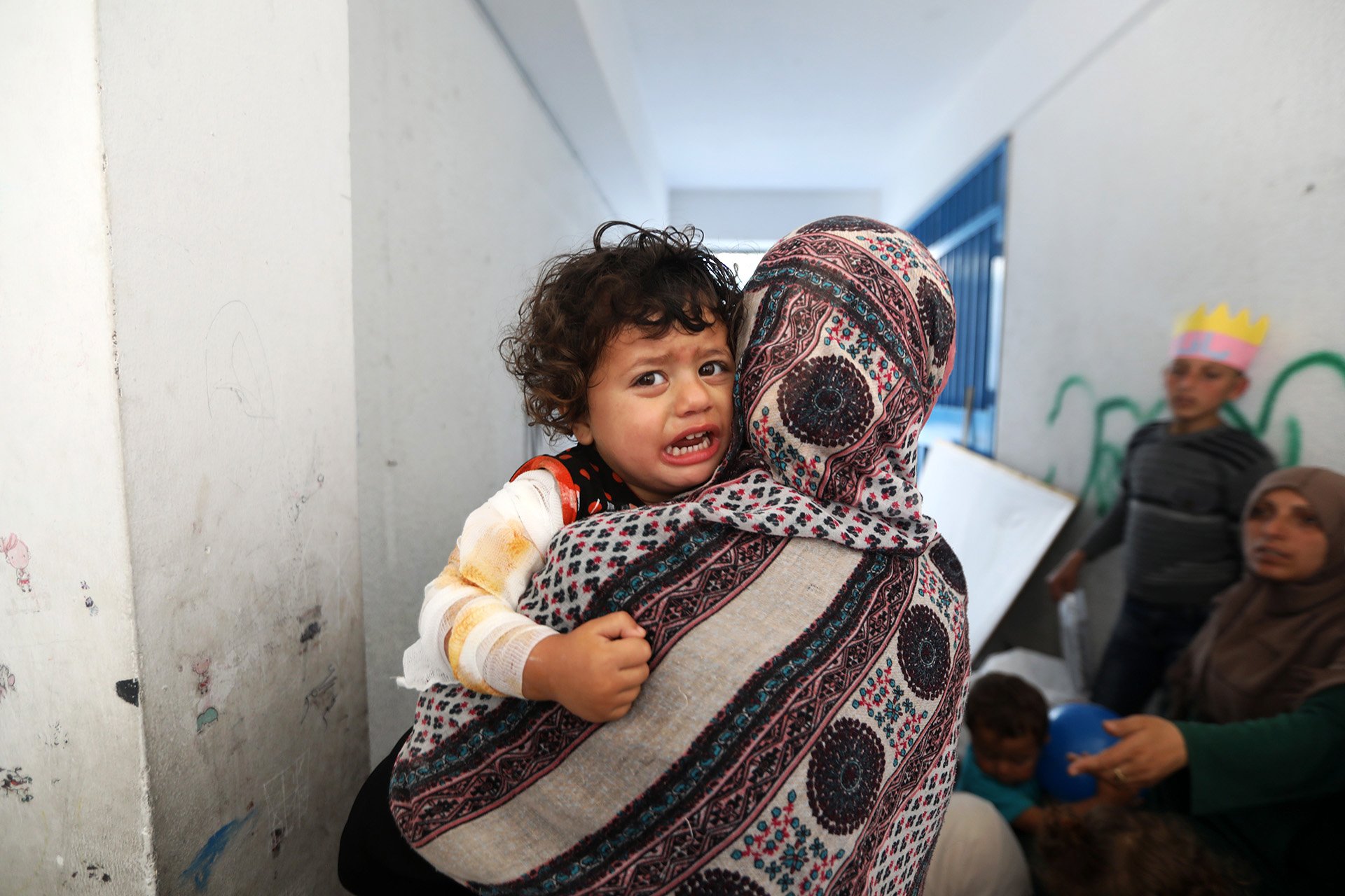 A woman holds a child who looks back at the camera in tears.