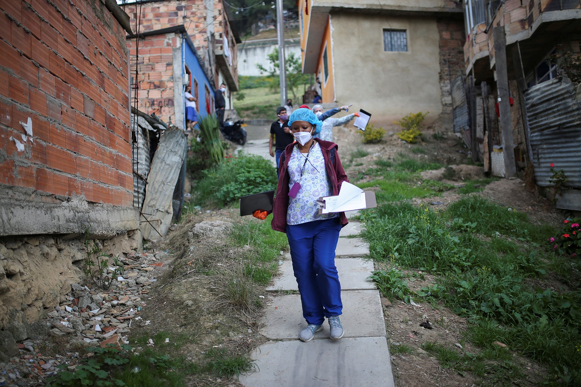 A woman in scrubs and a mask walks down a makeshift staircase in a suburb