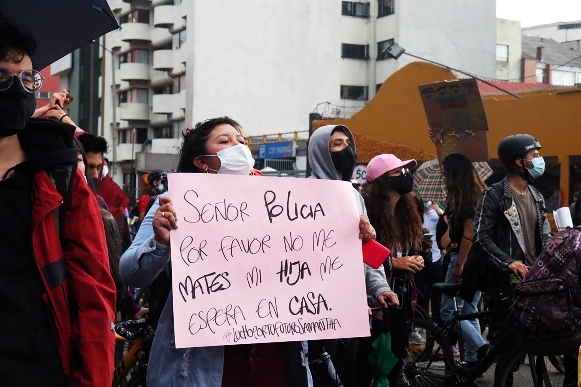 A woman wearing a mask holds a sign. 