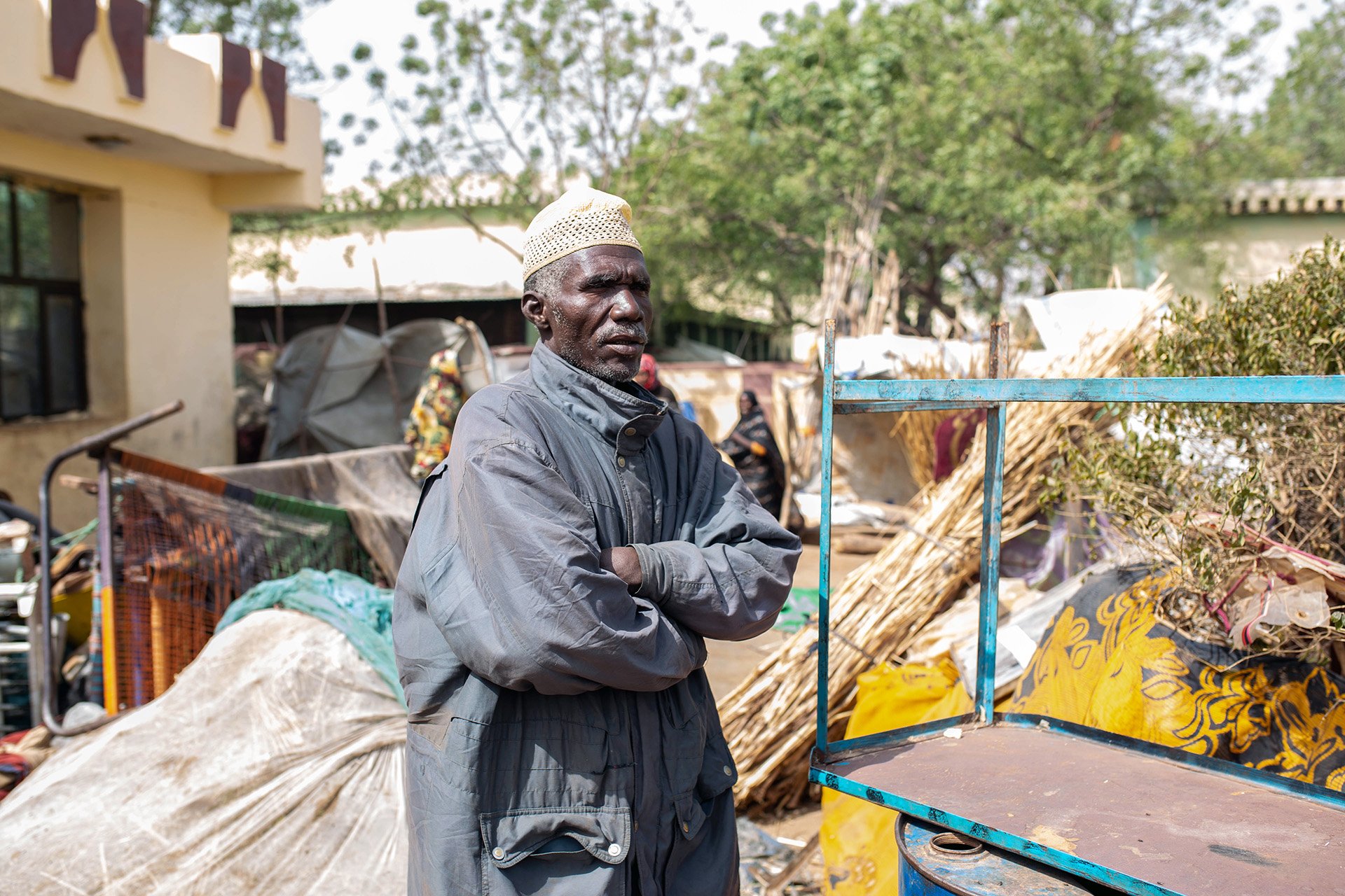 A man stands with his arms crossed in the mids of makeshift shelters.