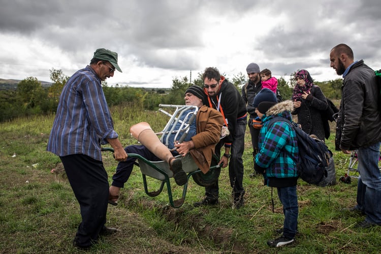 Disabled man carried over the bumpy ground to the border