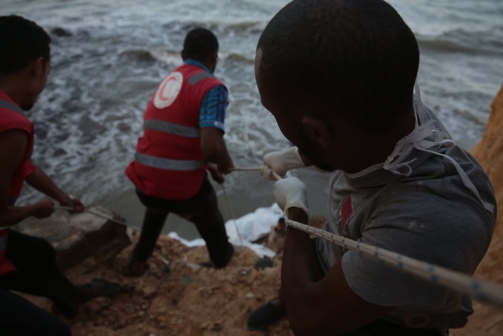 Red Crescent volunteers use ropes to pull a salvaged migrant body up the cliff-face on the beach at Tajoura - a Tripoli suburb