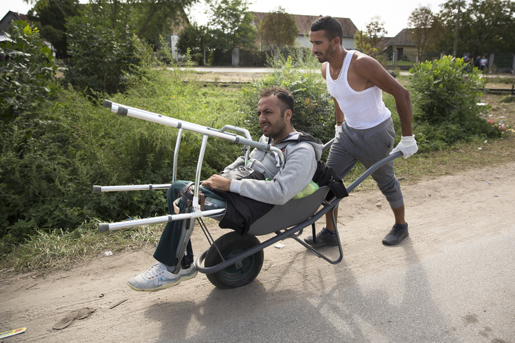 A man pushes his friend, who lost both his legs when ISIS attacked his university in Aleppo