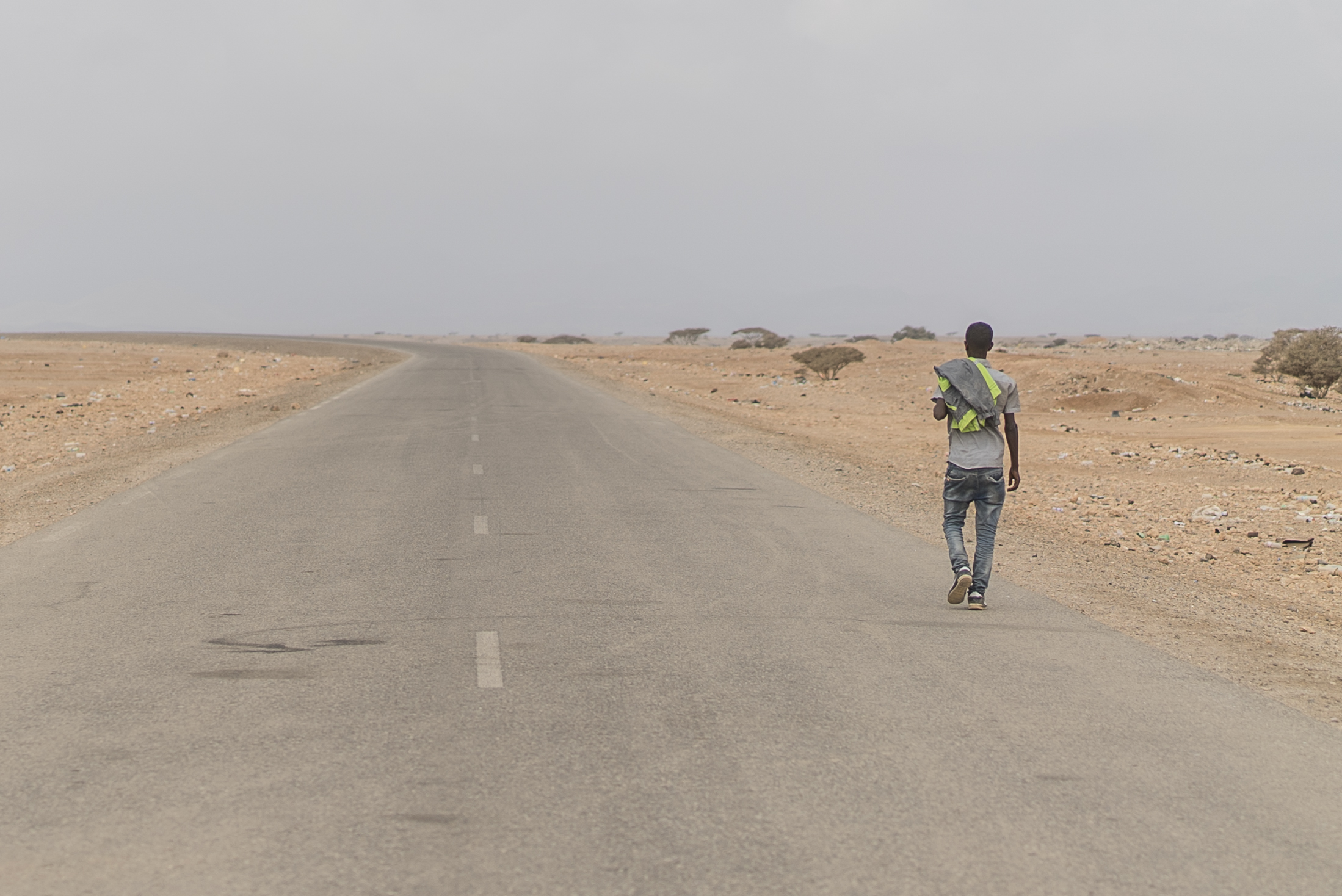 A man walks away from camera down an outstretched road in a desert scene