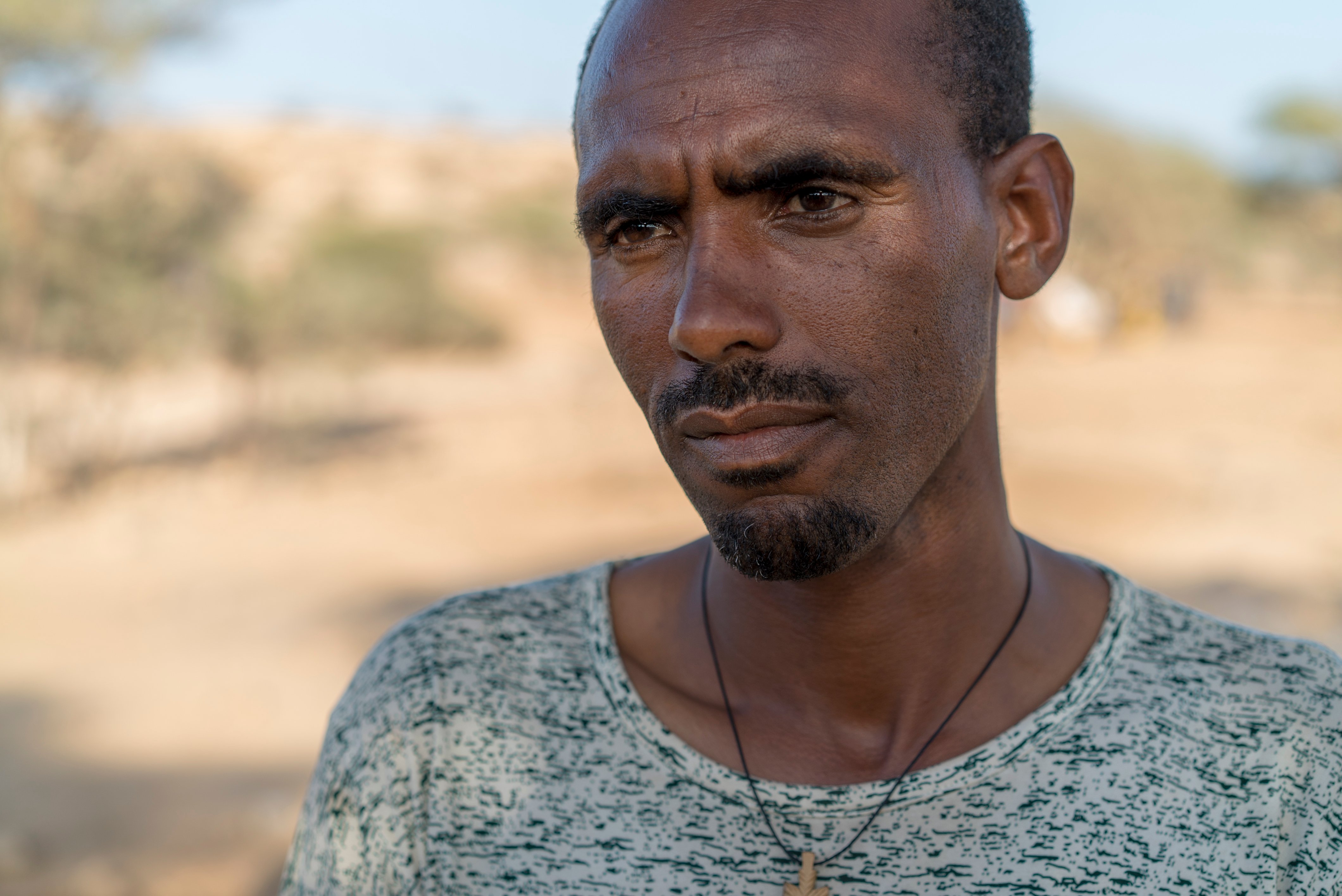 Portrait of a man looking off camera wearing a grey shirt and necklace