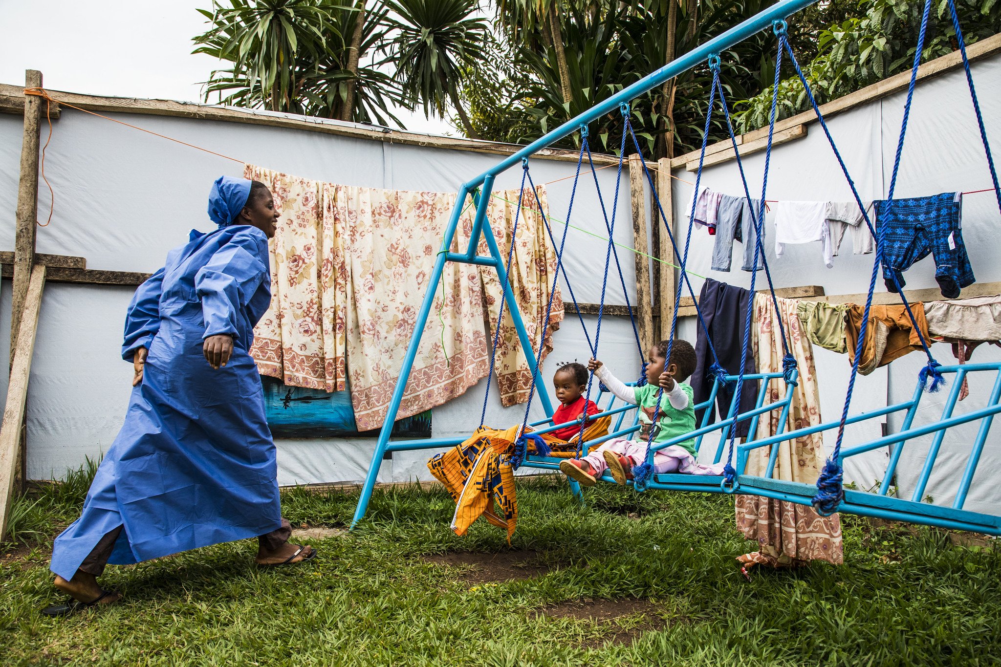 Two children on swings while a caregiver in scrubs looks on happily