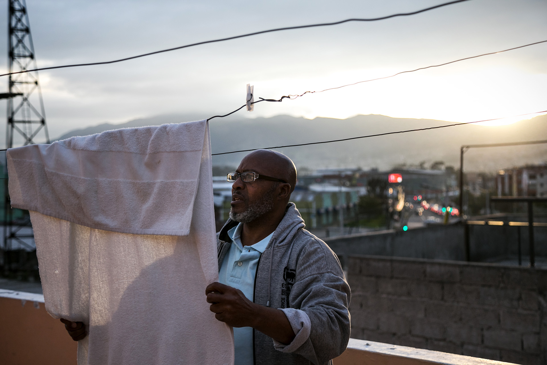 A photo of Orlando* hanging up his laundry on a terrace, with the sun setting in the background. 