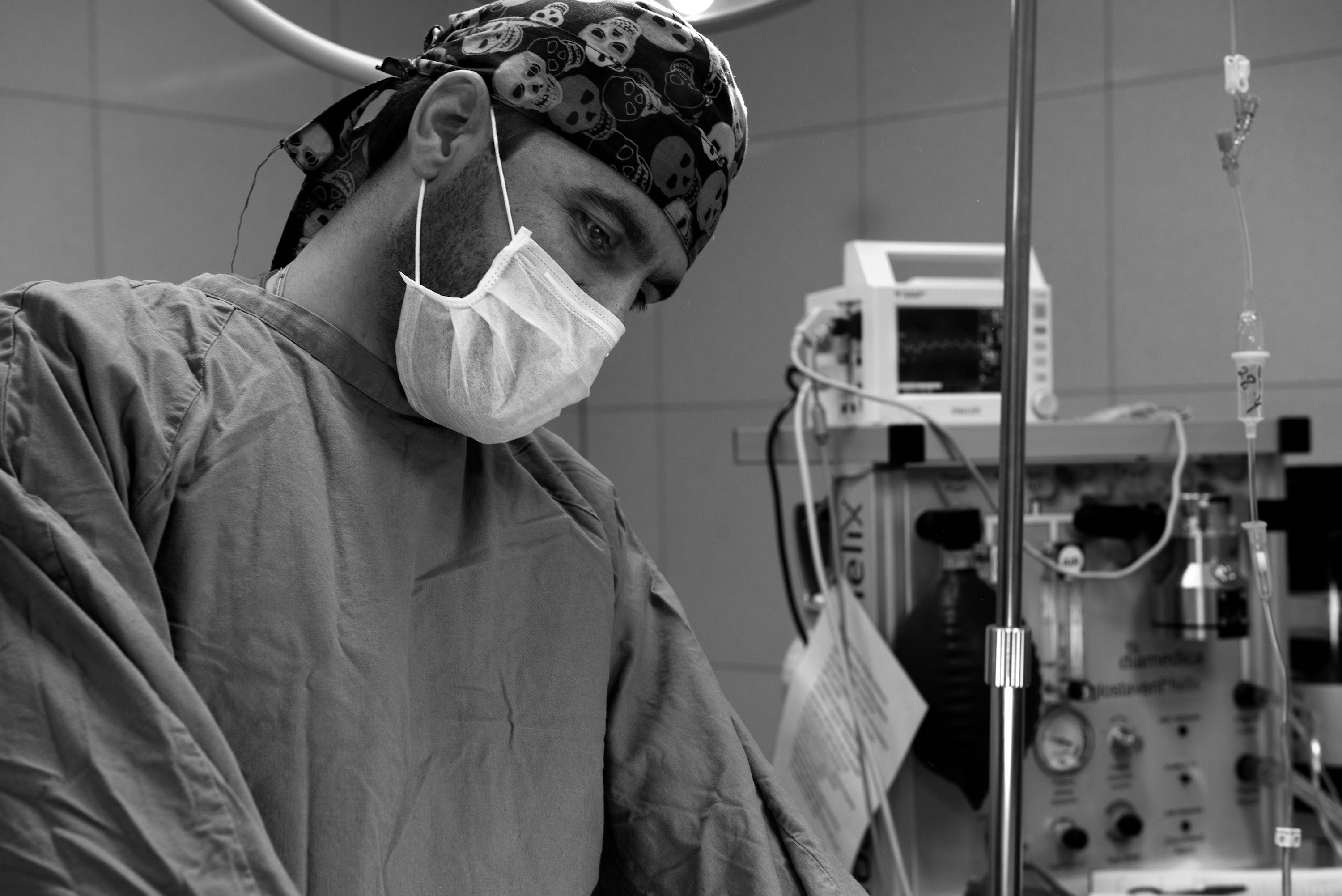 A black and white closeup of a doctor with a surgical face mask on.