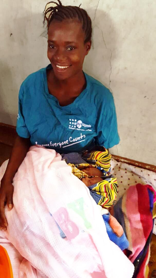 Portrait of a mother smiling and sitting against a wall holding her baby in a blanket