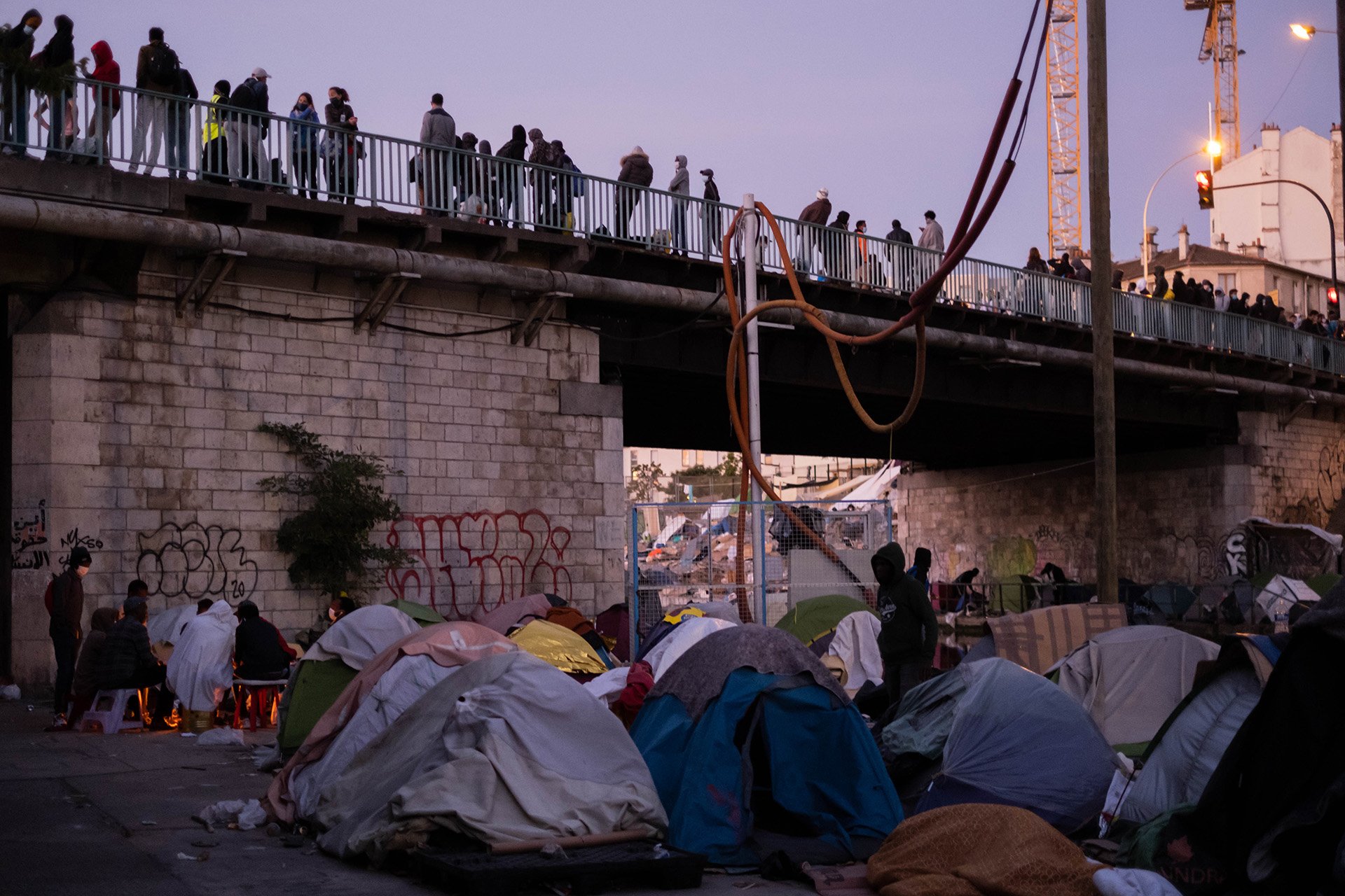 An image shows multiple tents set up along a city canal, under a bridge