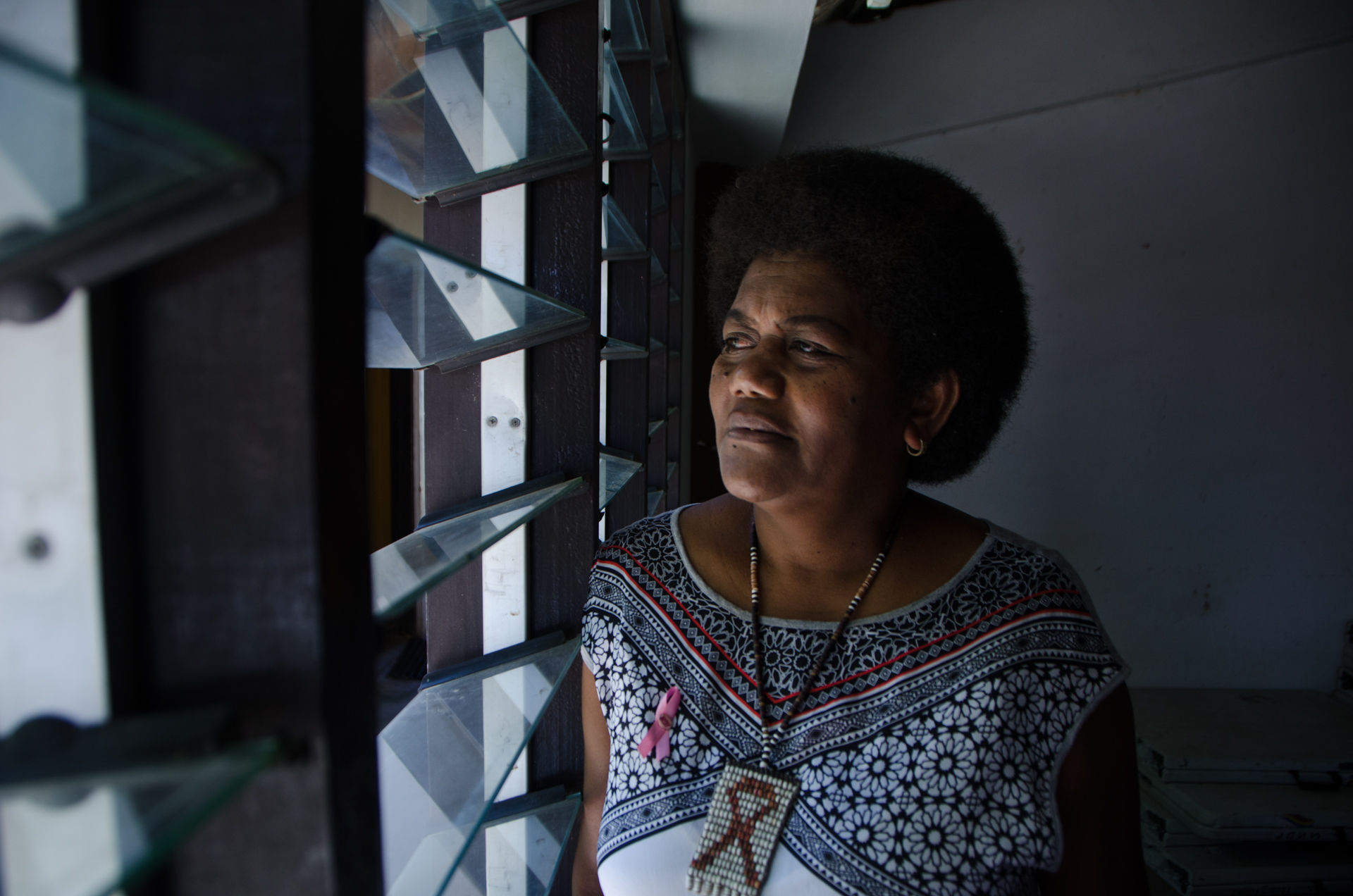 A woman looks out a slatted window.