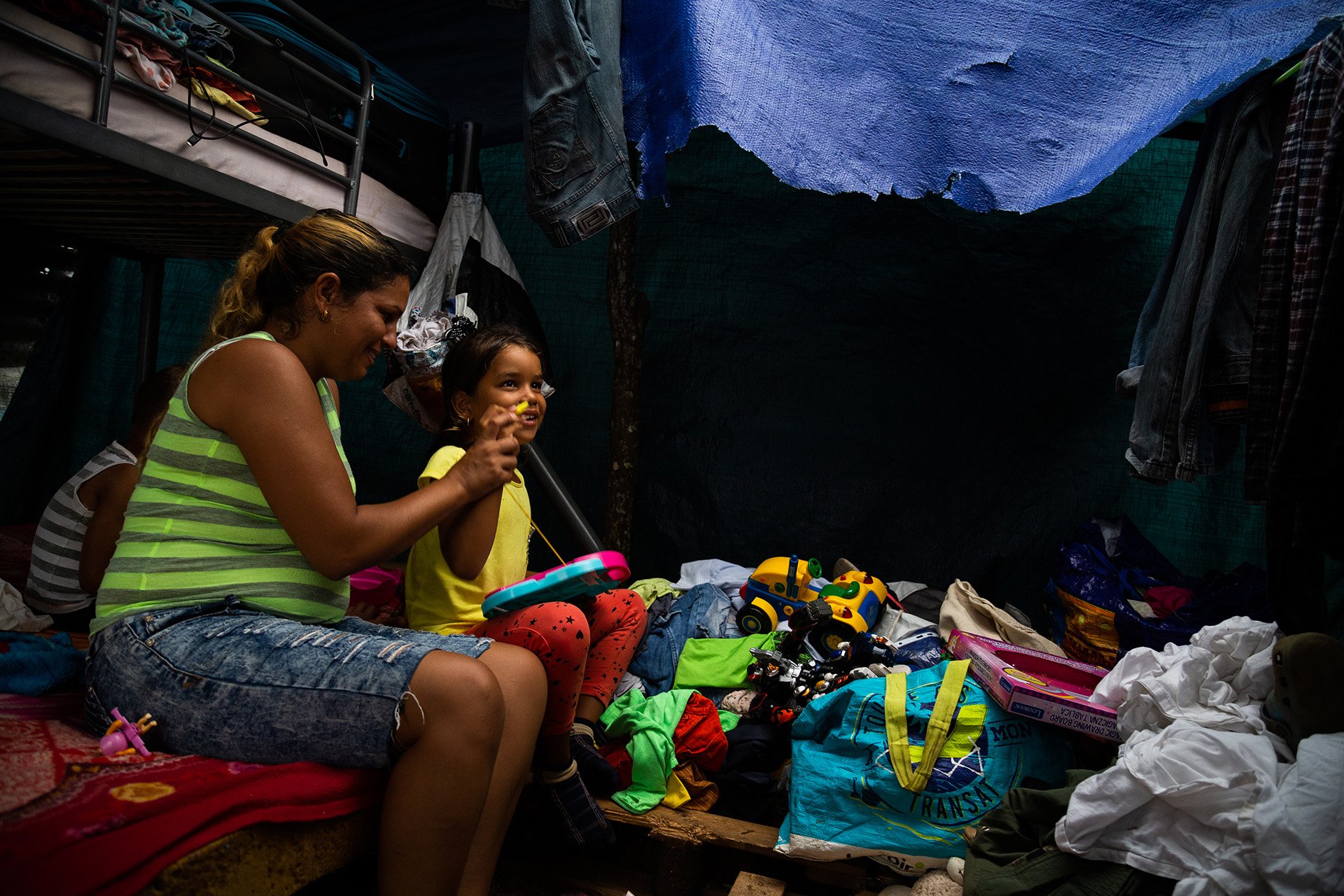 A young girl sits with her caretaker on the bottom bunk of a bunk bed. 