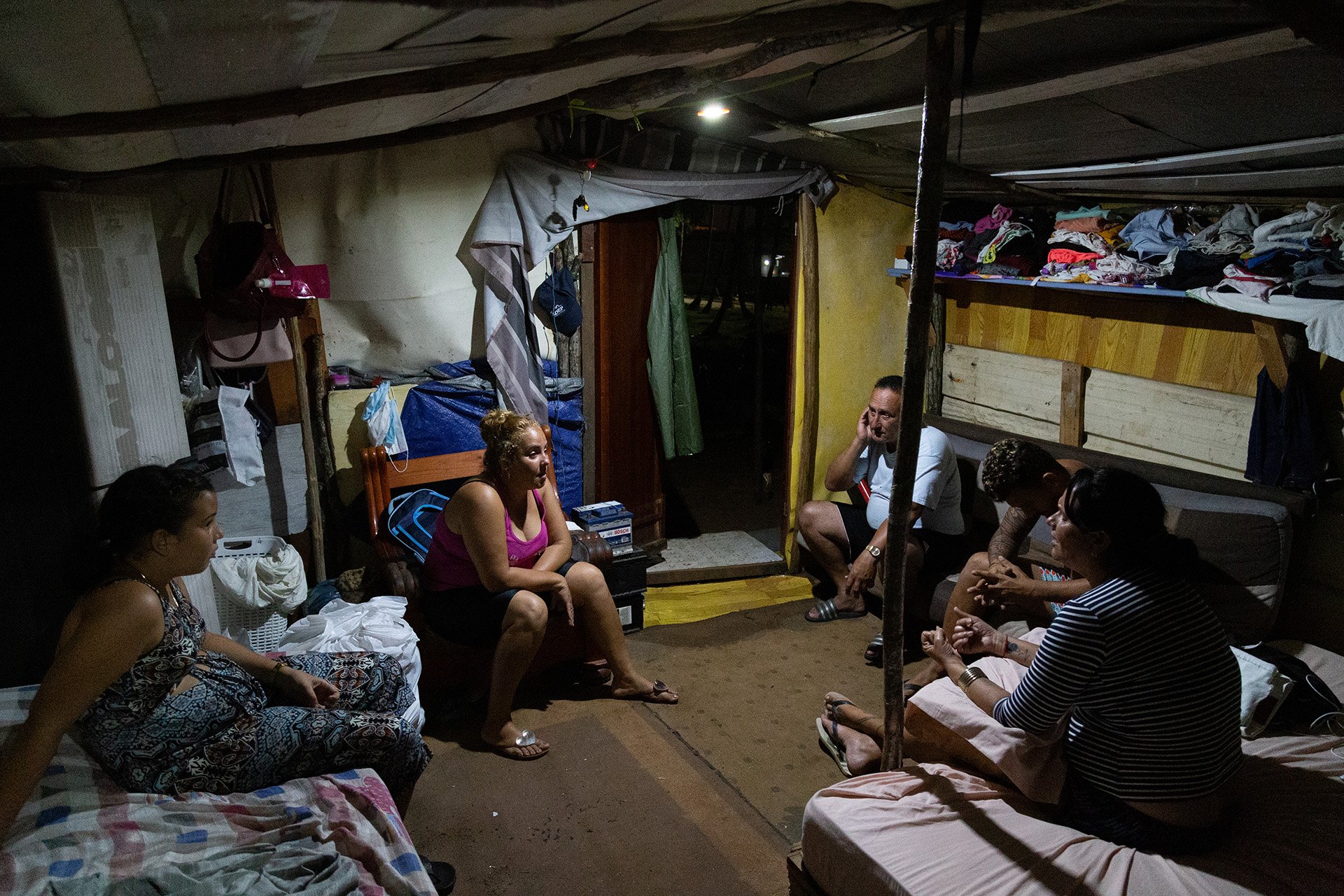 A family of Cuban migrants sits in a circle inside their tent talking in the evening. 