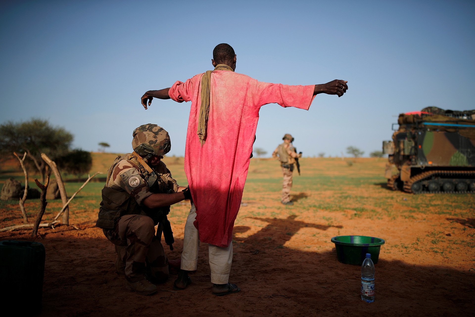 A soldier searches a man standing up, his back is to the camera.