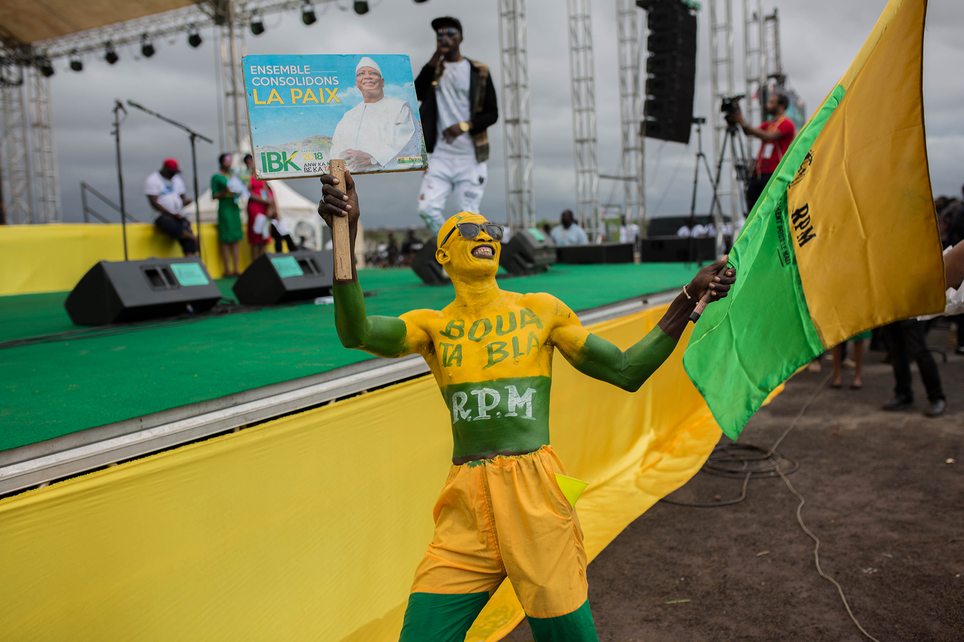 A person covered in green and yellow body paint waves a banner at a political rally.