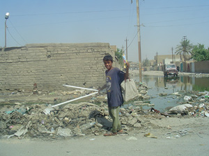 [IRAQ] A boy pulls flourescent light tubes out of the trash piled around the sewage in the street in Kamaliya, a poor suburb of Baghdad.