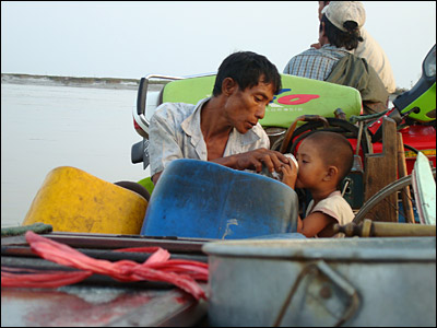 A father giving his son something to drink as they sit on board a ferry. Lack of safe drinking water is a major problem and reports of diarrhoea are increasing.