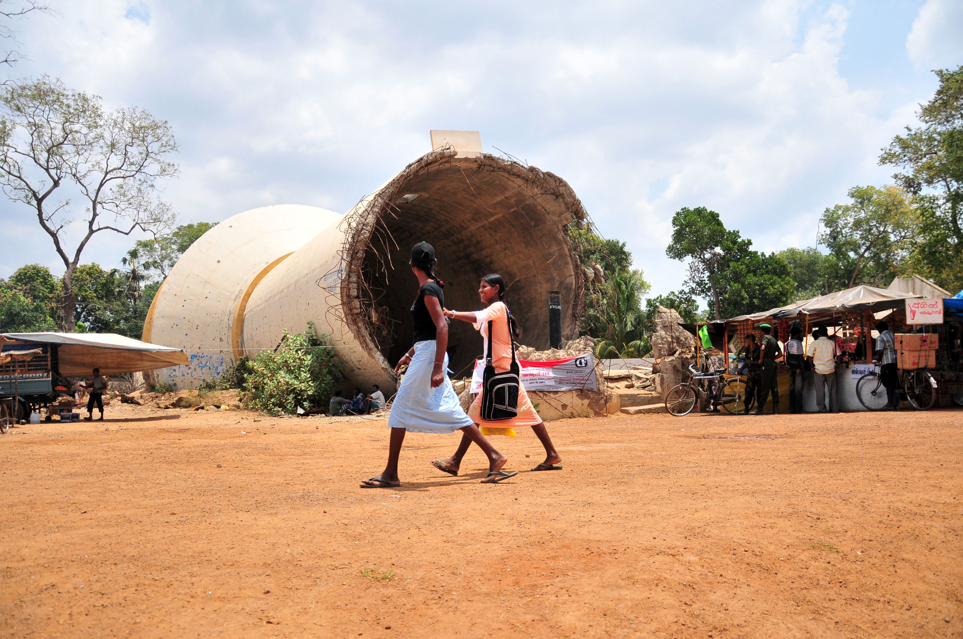 Two women walk by a water tank destroyed by the LTTE in Kilinochchi, the former capital of the rebel group.