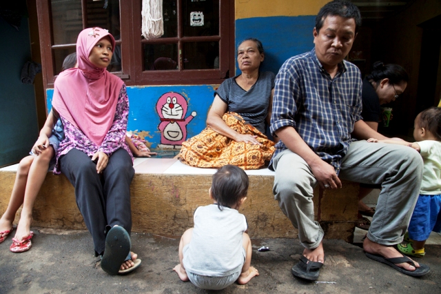 A family sits in an alleyway outside their homes along the Ciliwung River in Jakarta. Flood waters in January rose to the top of the first floor of their houses