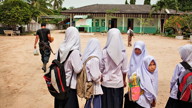 A paramilitary Ranger with groceries walks by students at Pakaluesong Elementary School in southern Thailand. About 30 Rangers live in a camp established in the school grounds.