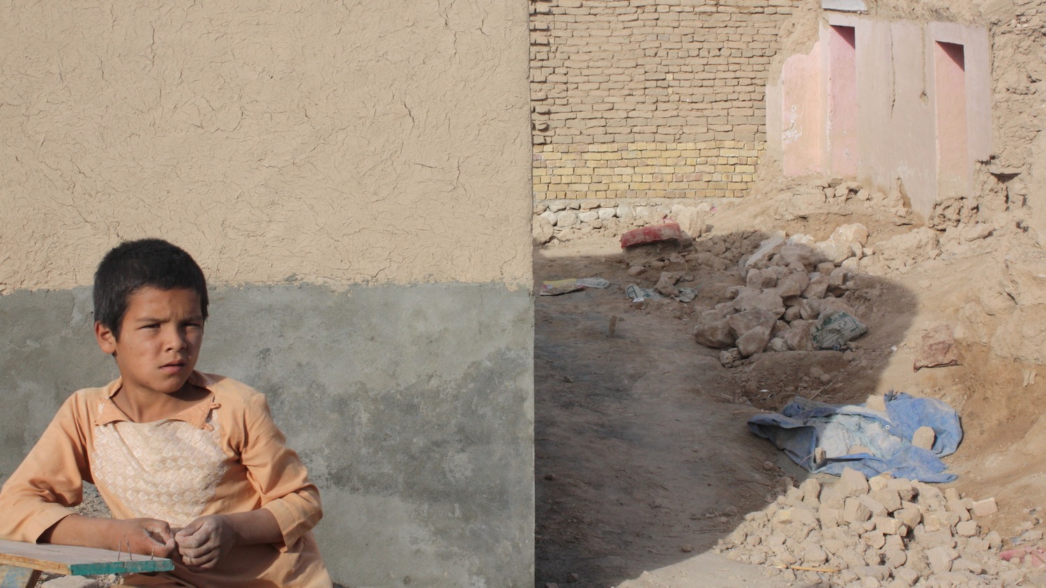 A child in northern Afghanistan sits in front of his former home, which was destroyed in floods in Spring 2014.