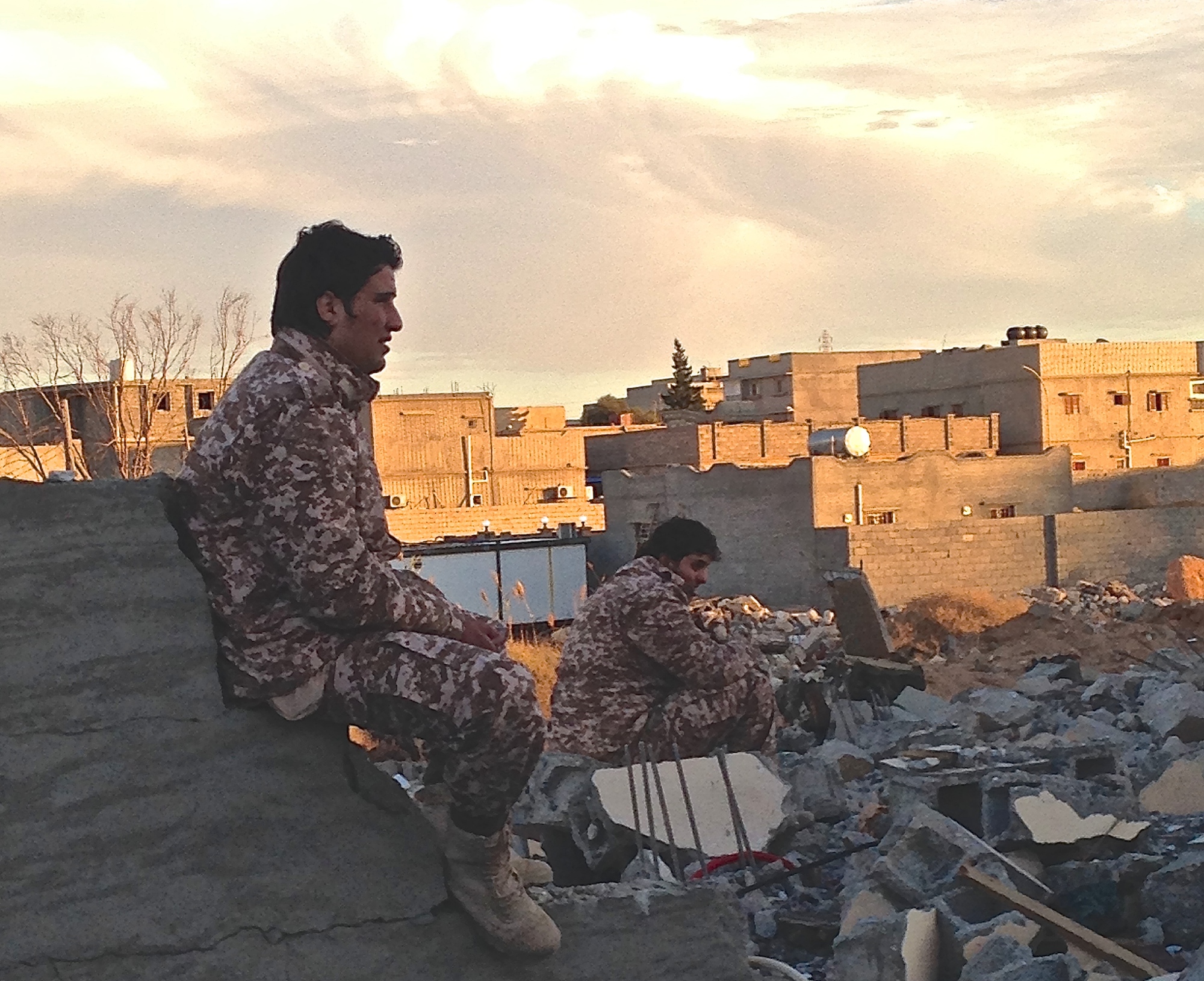 NOT FOR REUSE Dusk in the Libyan town of Ben Jawad, where two soldiers from forces operating under the Tripoli-based government sit by the rubble of another flattened home. The front-line, near Es Sidra oil port, is just 30 kilometres away.