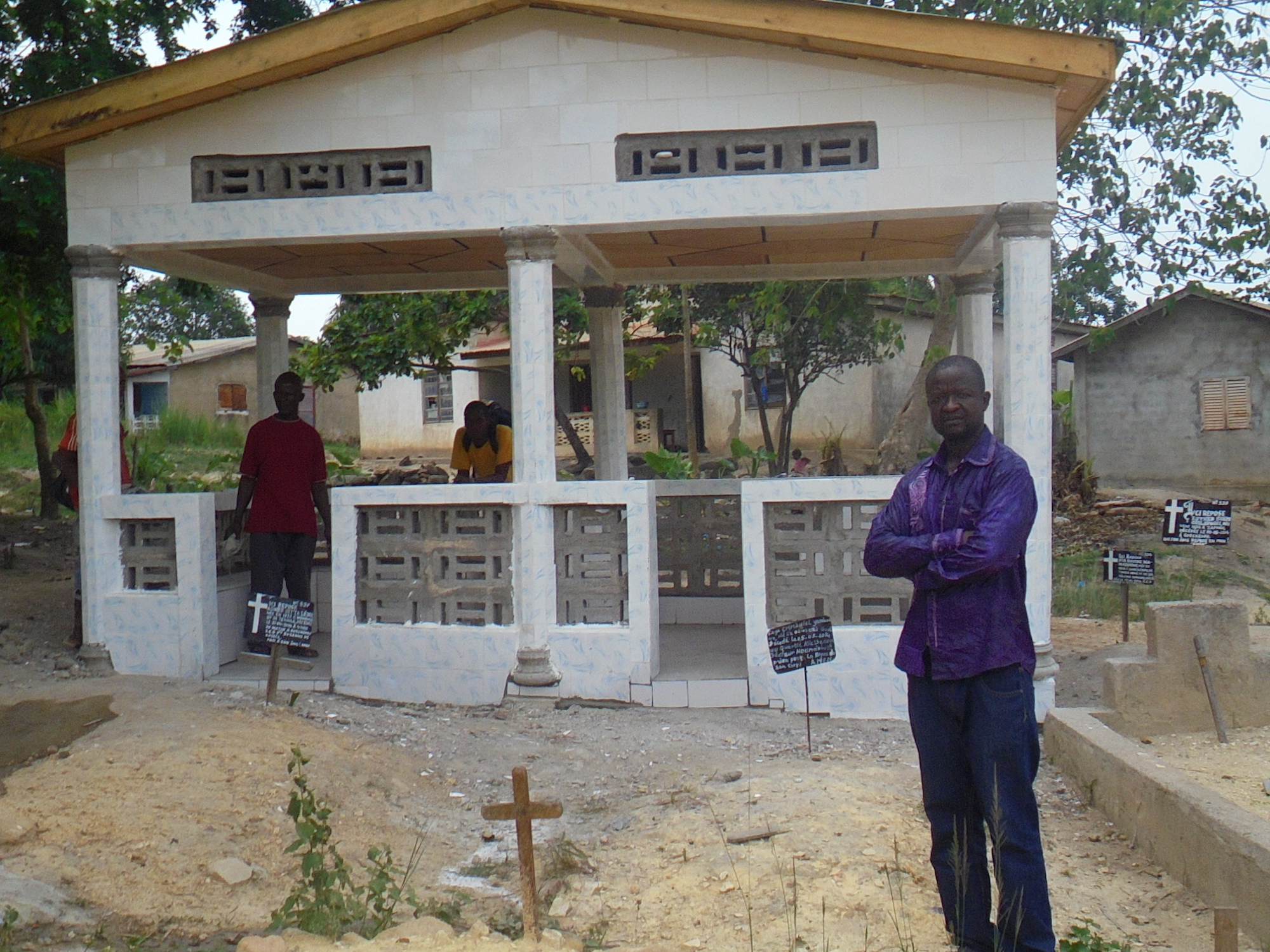 Maurice Ouendeno (on the right) stands outside the memorial sanctuary they built for his father in lieu of having a real burial plot. Guineans, like Maurice, waited more than a year to bury loved ones who had died from Ebola due to the clash between gover