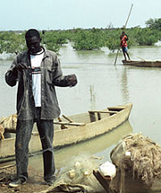 [Burkina Faso] A fisherman in Sandogo, Burkina Faso, inspects his nets as a fellow villager poles his boat in the background.