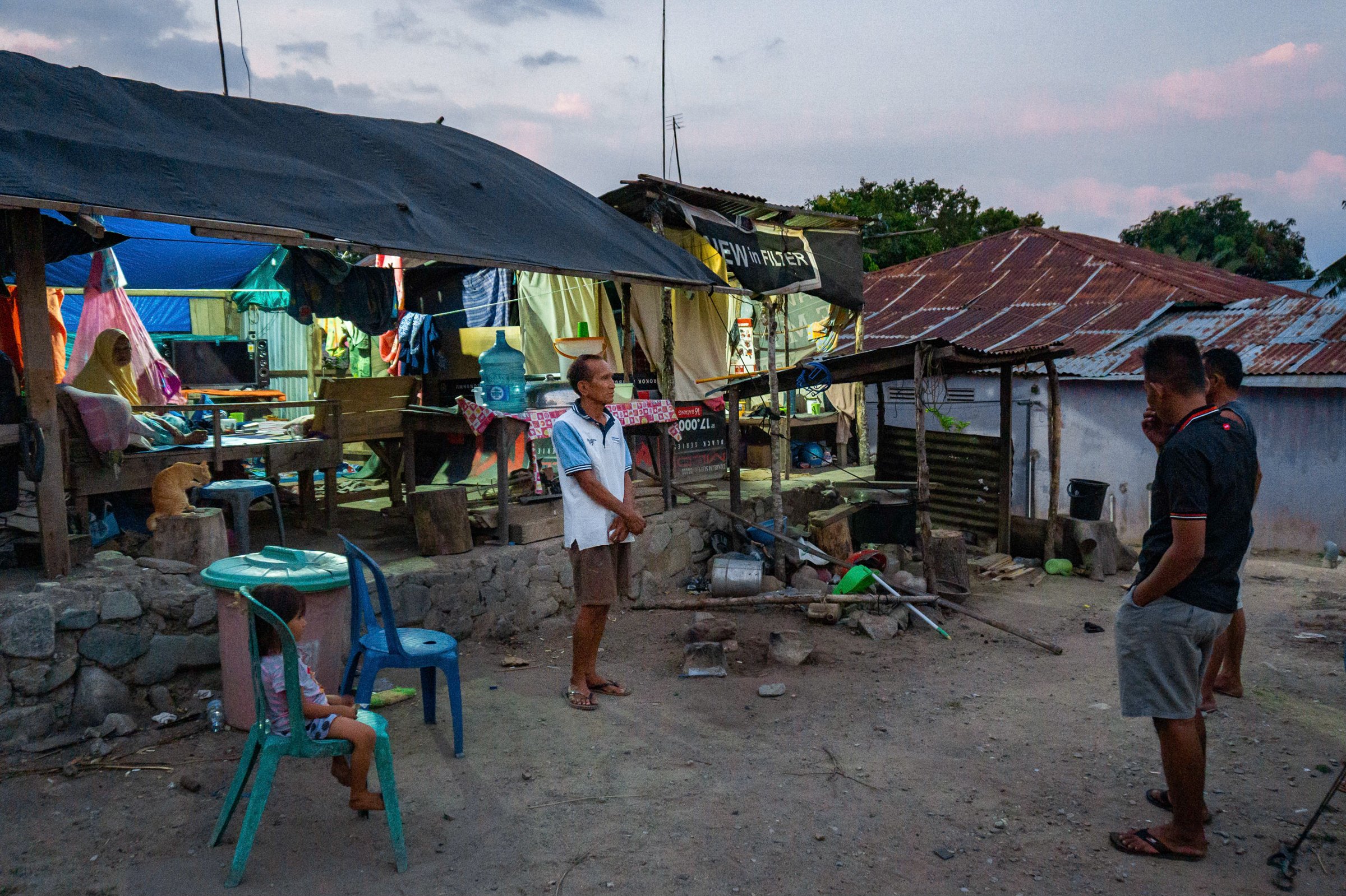 Hamsin Lasaso stands outside his damaged home and the tarp-and-wood structure that now shelters his family in Indonesia.