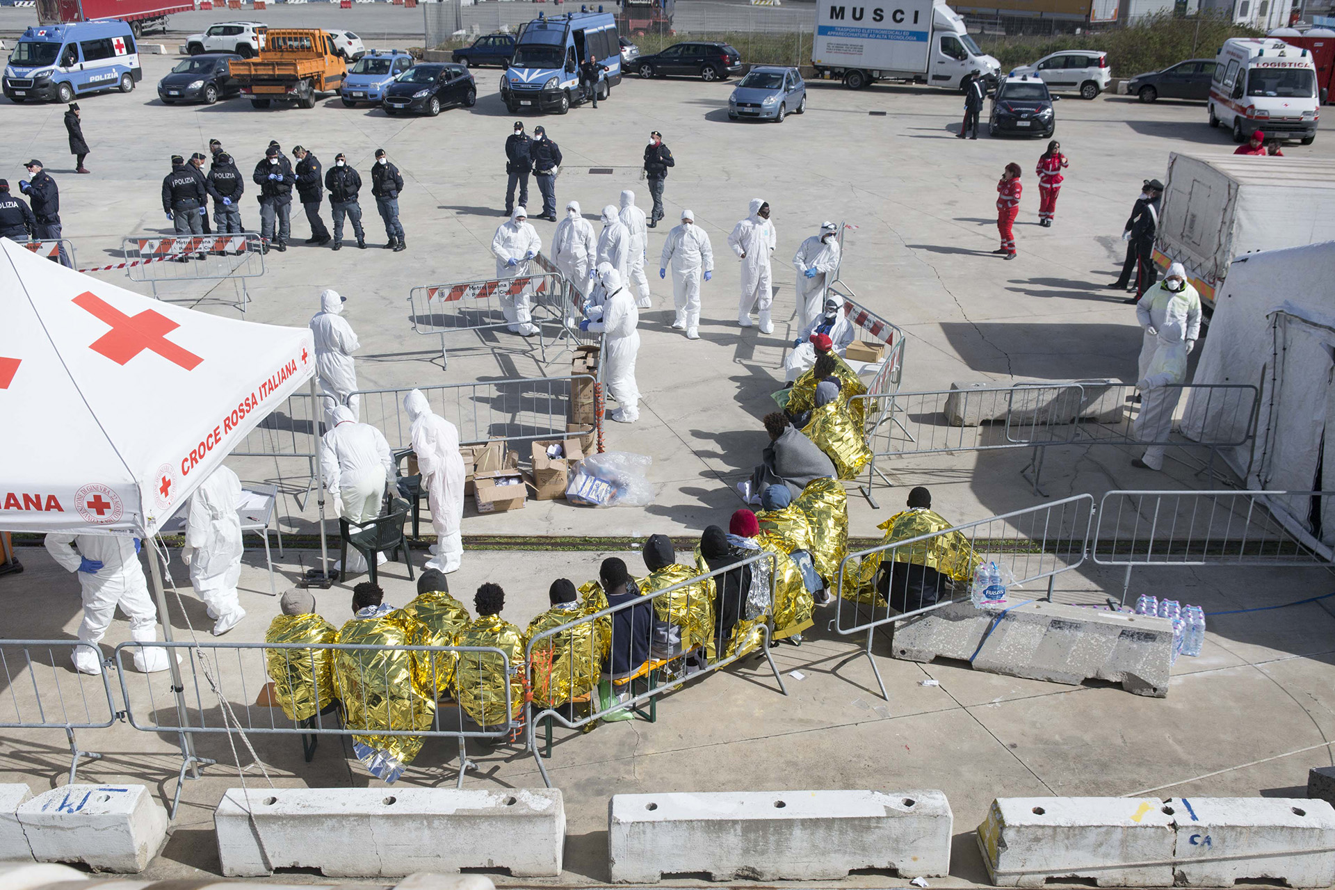 Image of migrants and asylum seekers sitting and waiting for a bus into the port of Messina