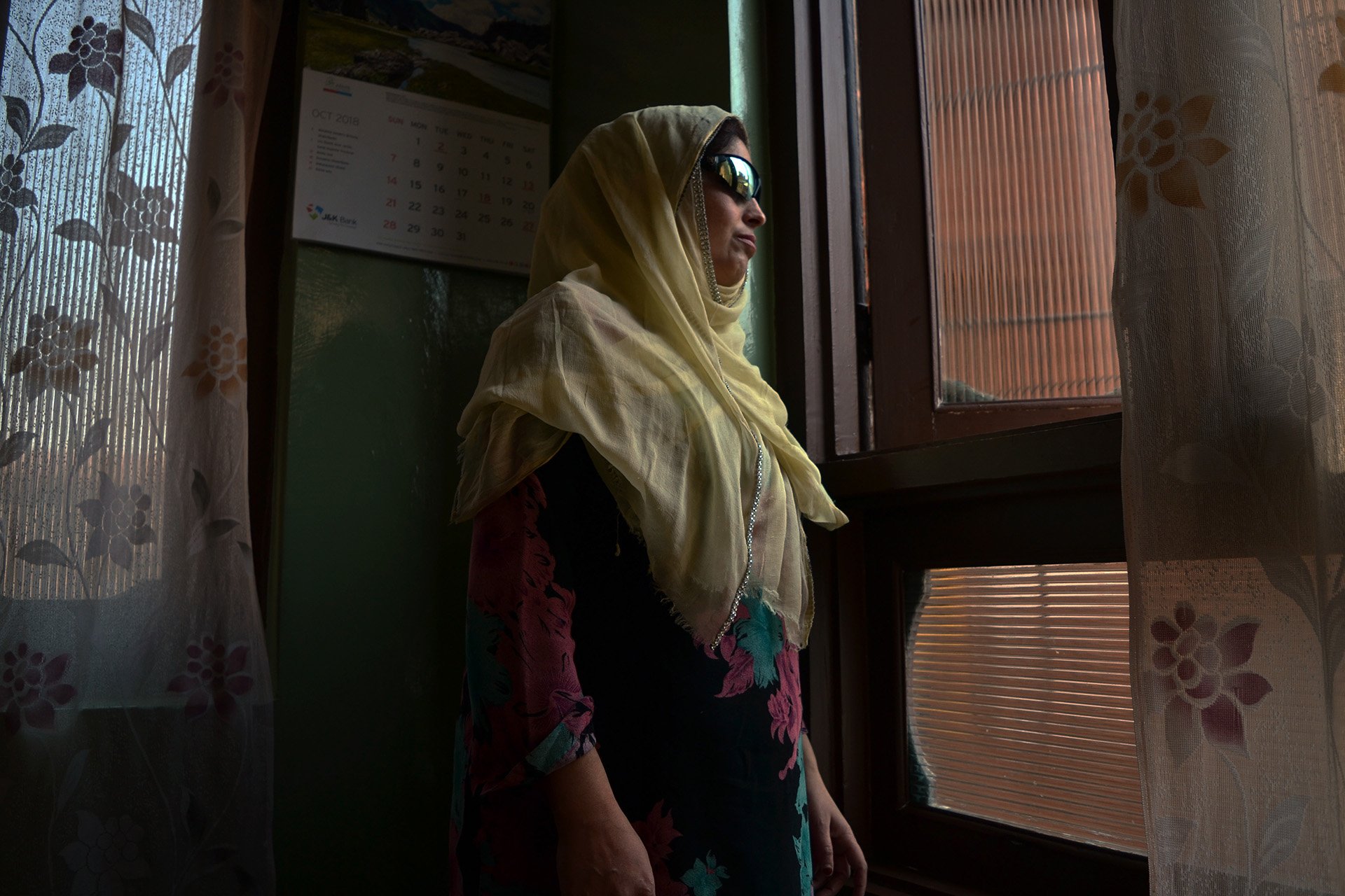 Nusrat Jan peers out a window at her home in Srinagar