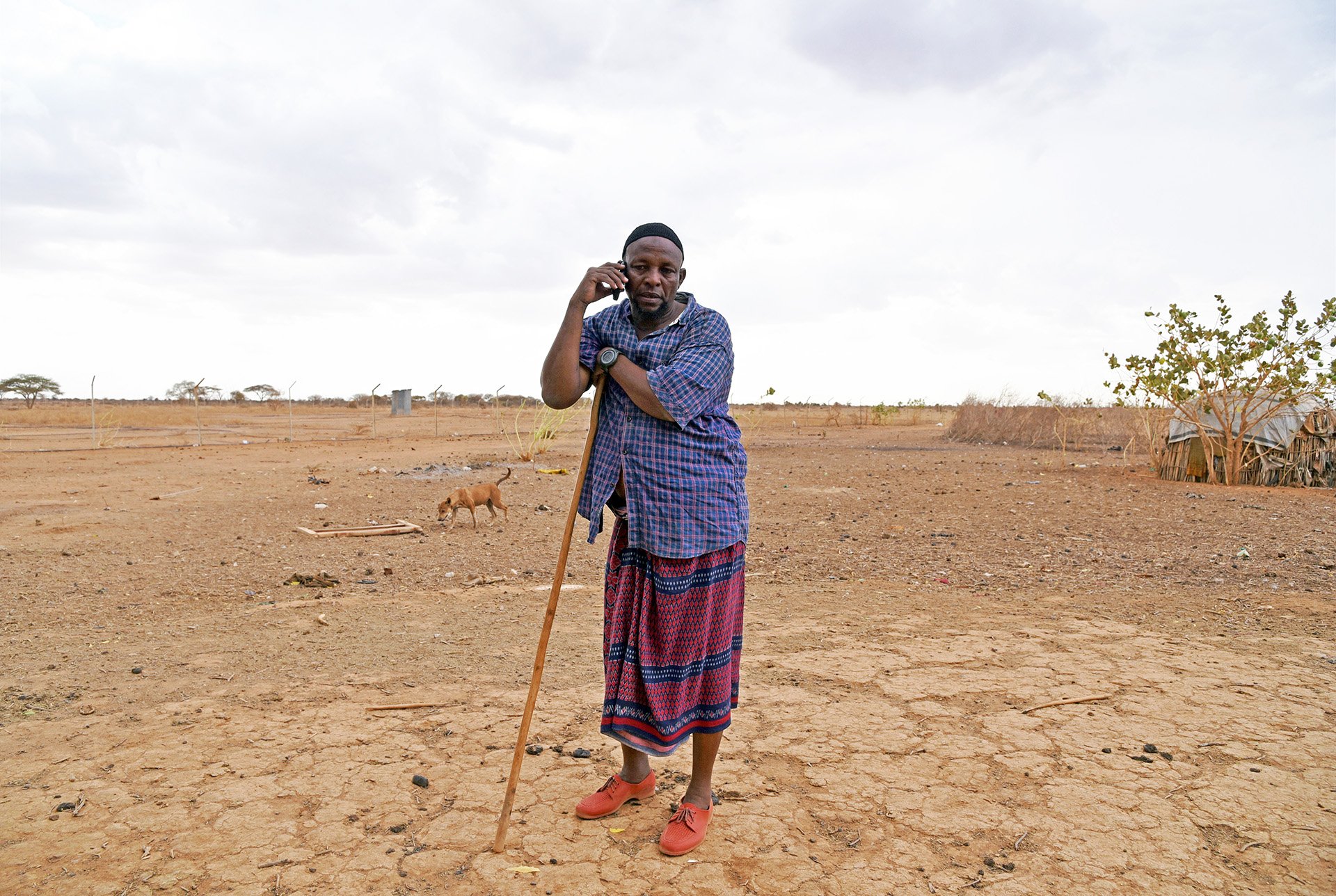 A man stands leaning on a staff in a dry plain.