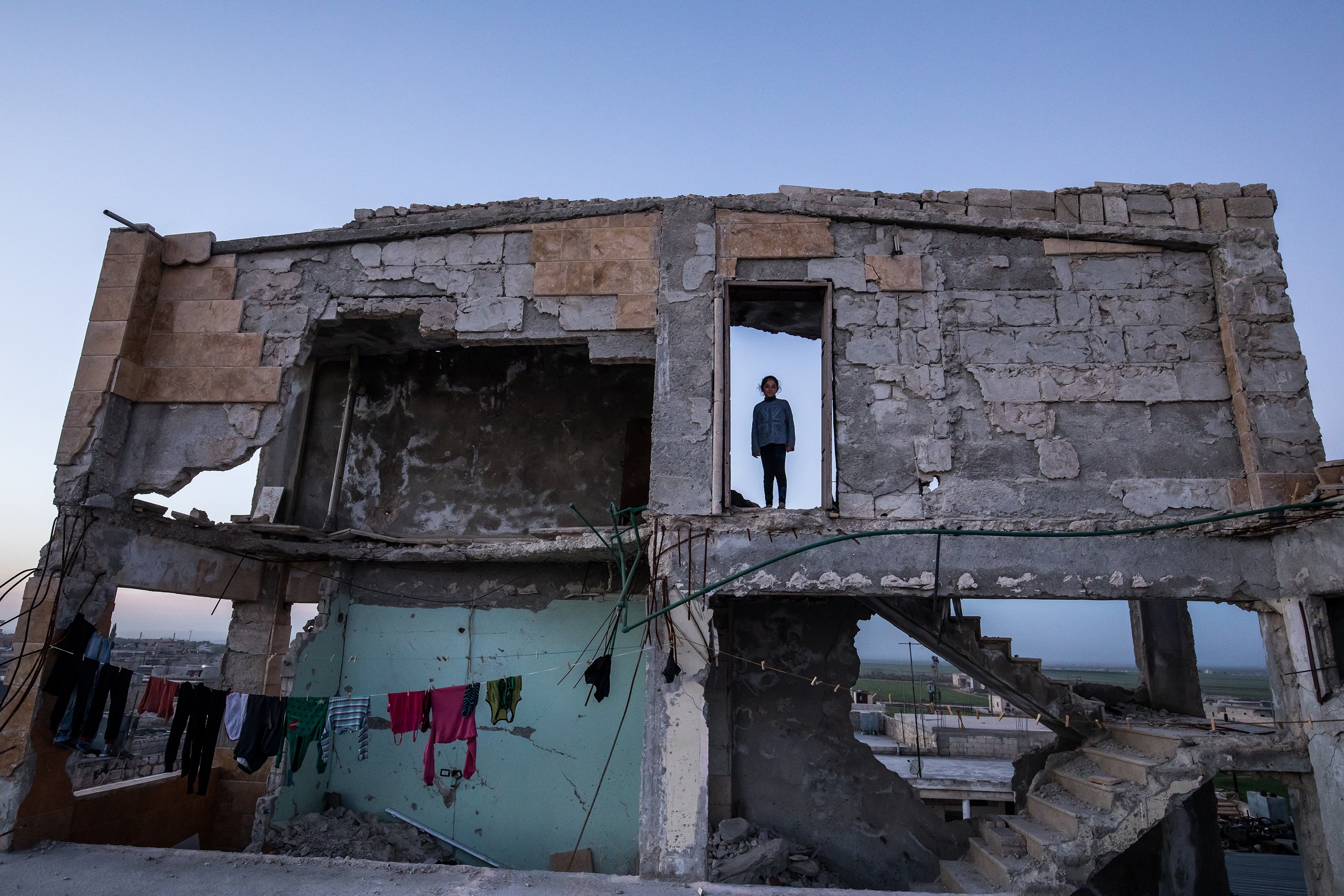 An exterior face of a destroyed building with the silhouette of a young girl in an open doorway on the second floor