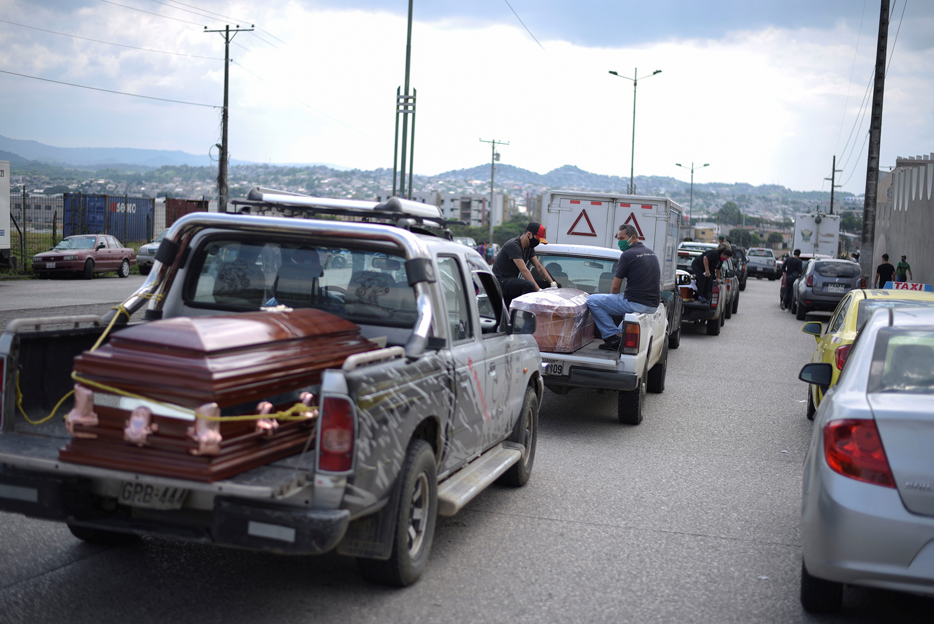 Vehicles carrying coffins lined up outside of a cemetery in Guayaquil