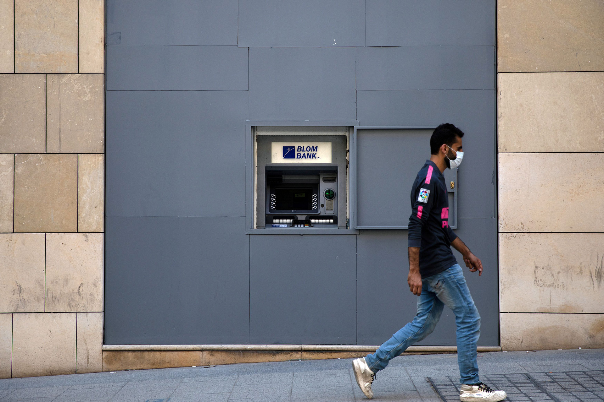 A man wearing a face mask walks past a fortified ATM machine during a partial lockdown in the Lebanese capital of Beirut, on 21 August 2020.