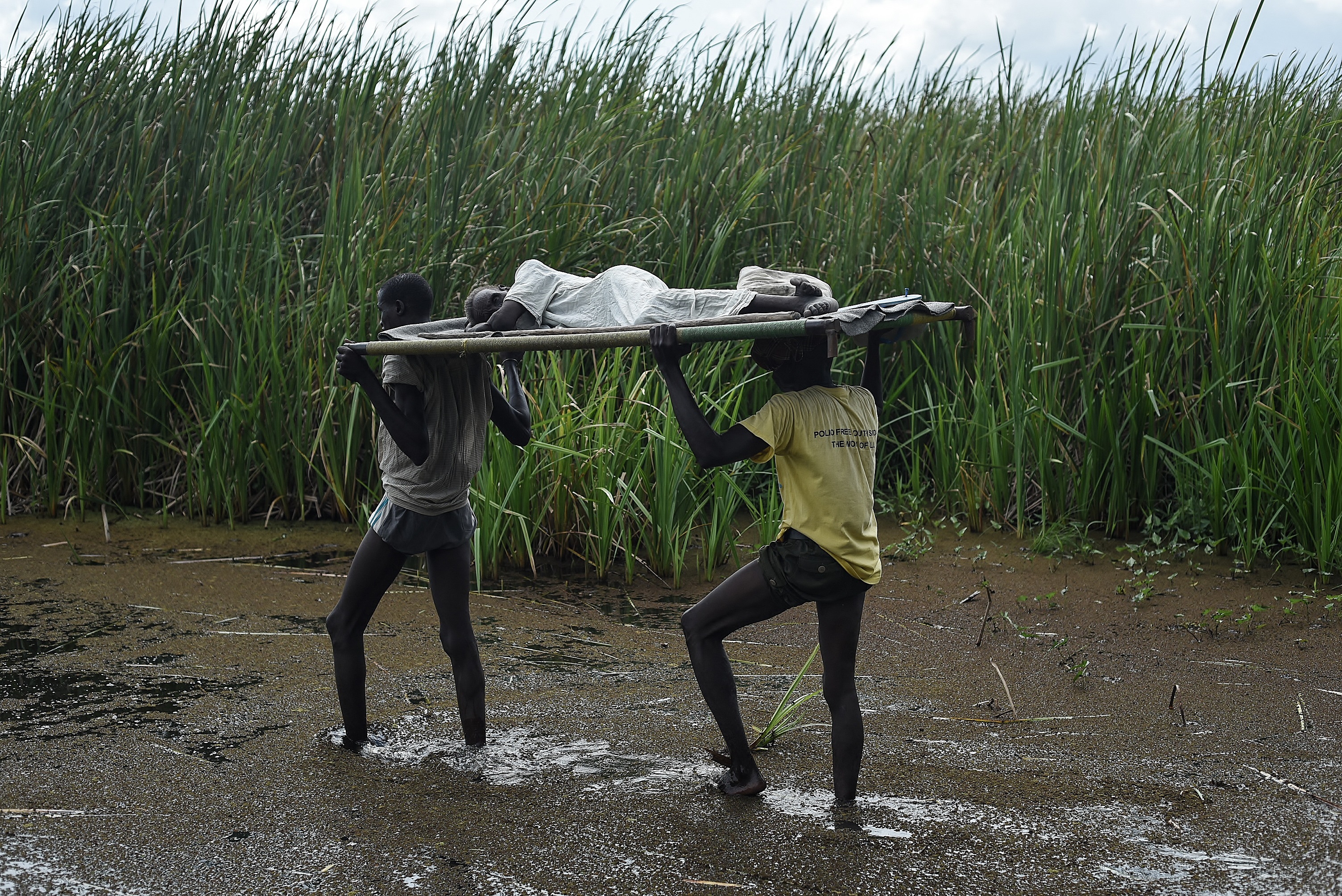 Men carry an elderly woman through the swamps