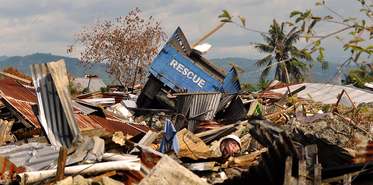 A truck labelled "rescue" buried and upturned in rubble.