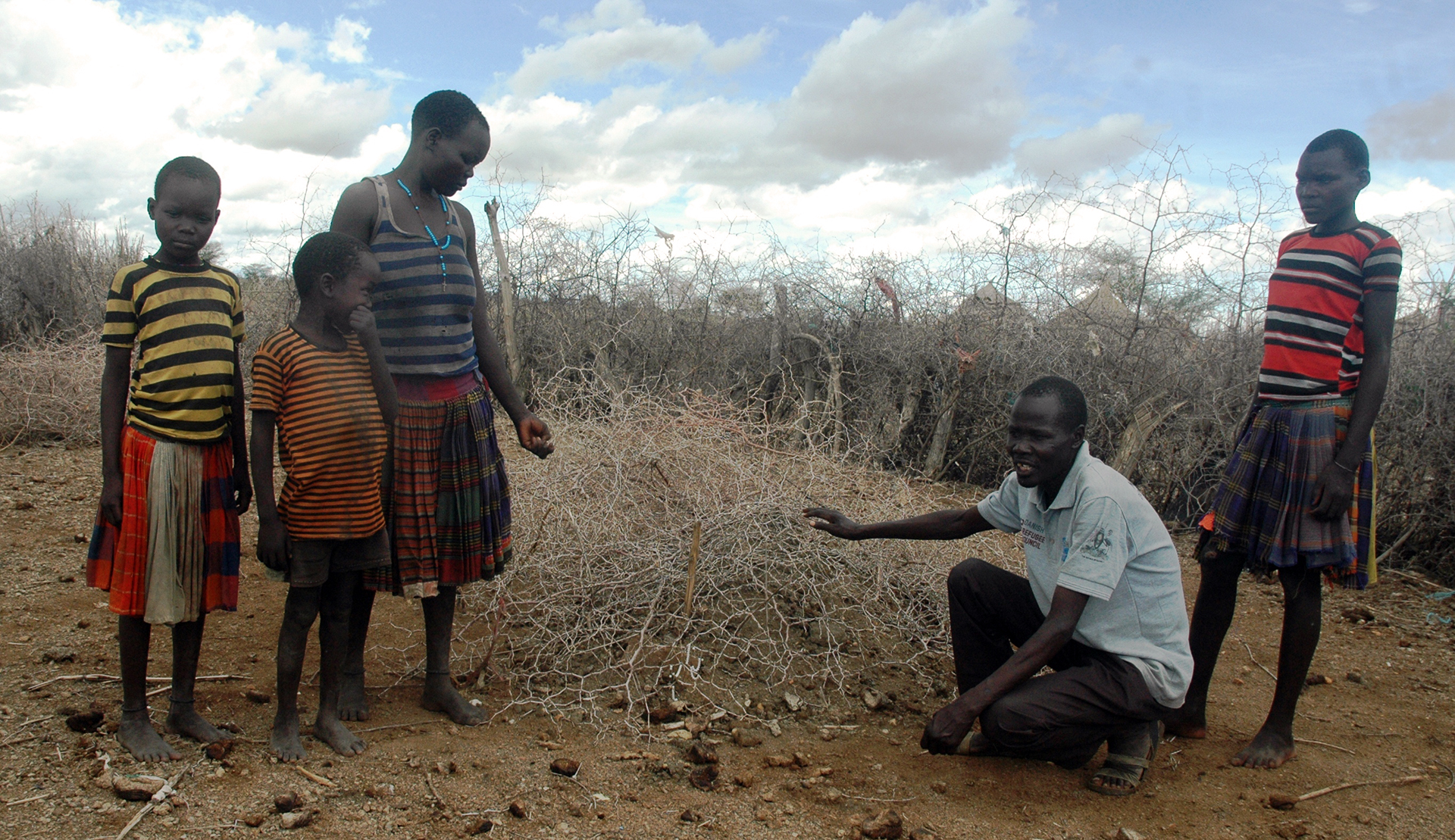 Photo of two adults and some children standiing by an unmarked grave in Uganda