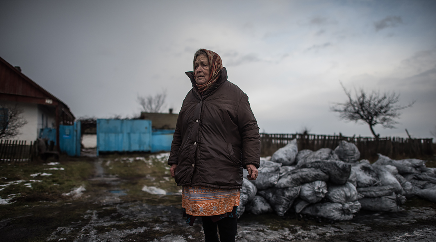 An elderly woman stands in the winter in Ukraine near the contact line of conflict.