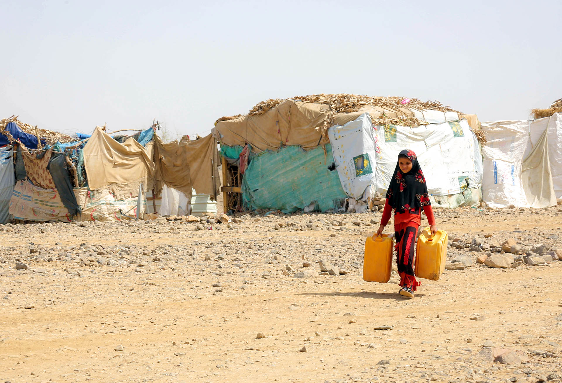 Photo of a young girl in Yemen with a watering can at a dry camp for displaced people.