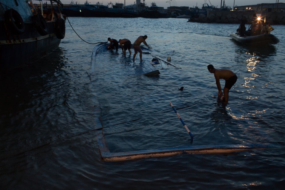 Volunteers remove trapped bodies of migrants from a capsized boat