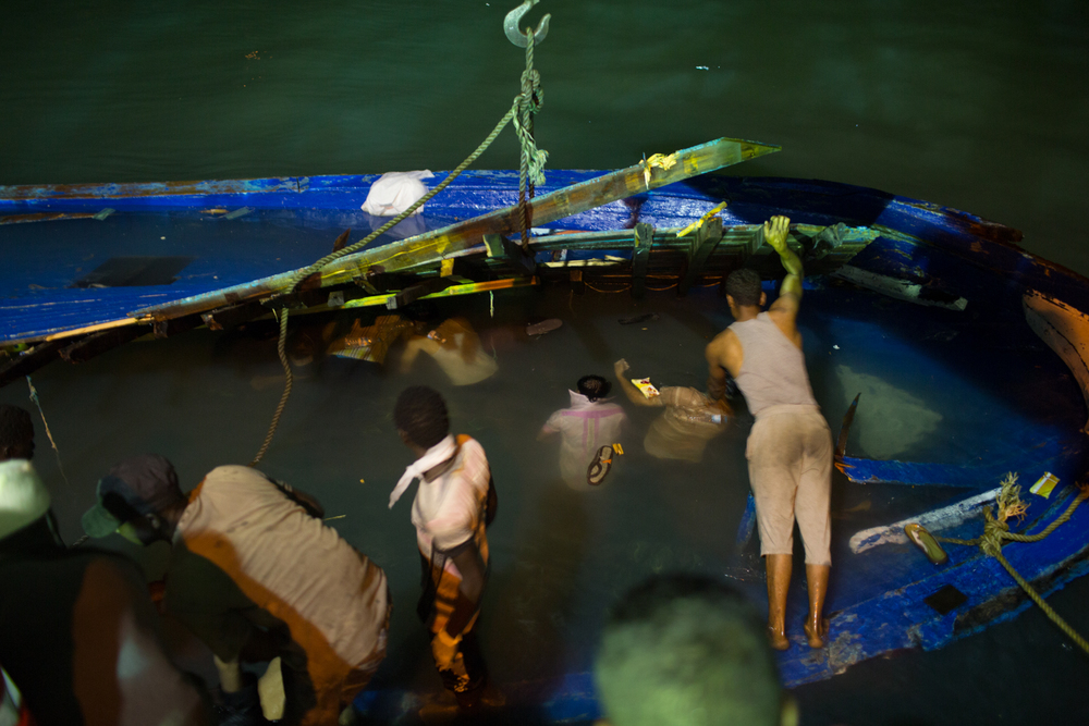 Volunteers remove trapped bodies of migrants from a capsized boat