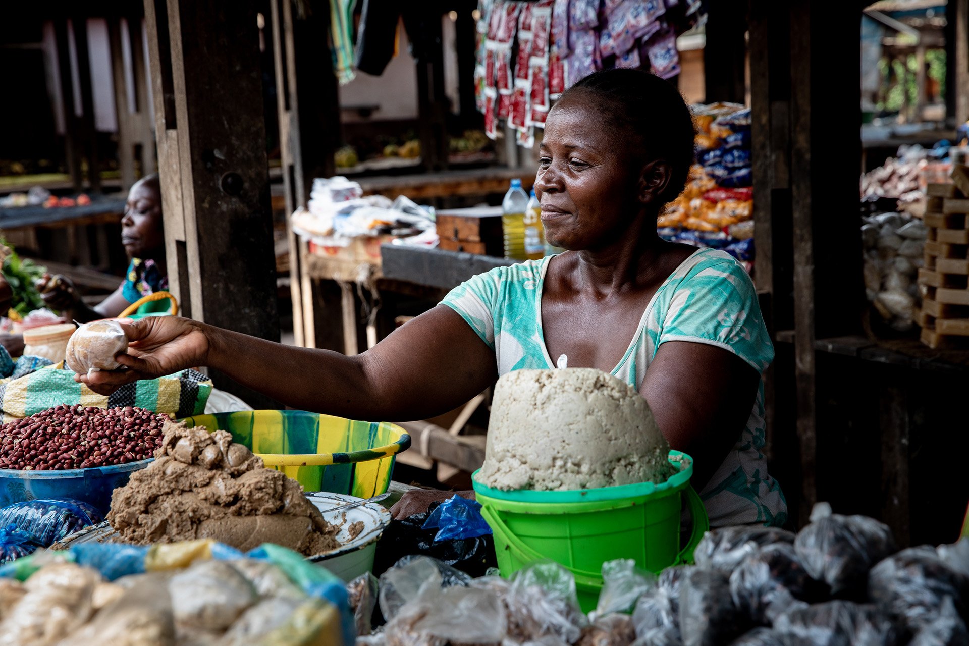 A woman helps a customer leaning across the counter of a food stall. 