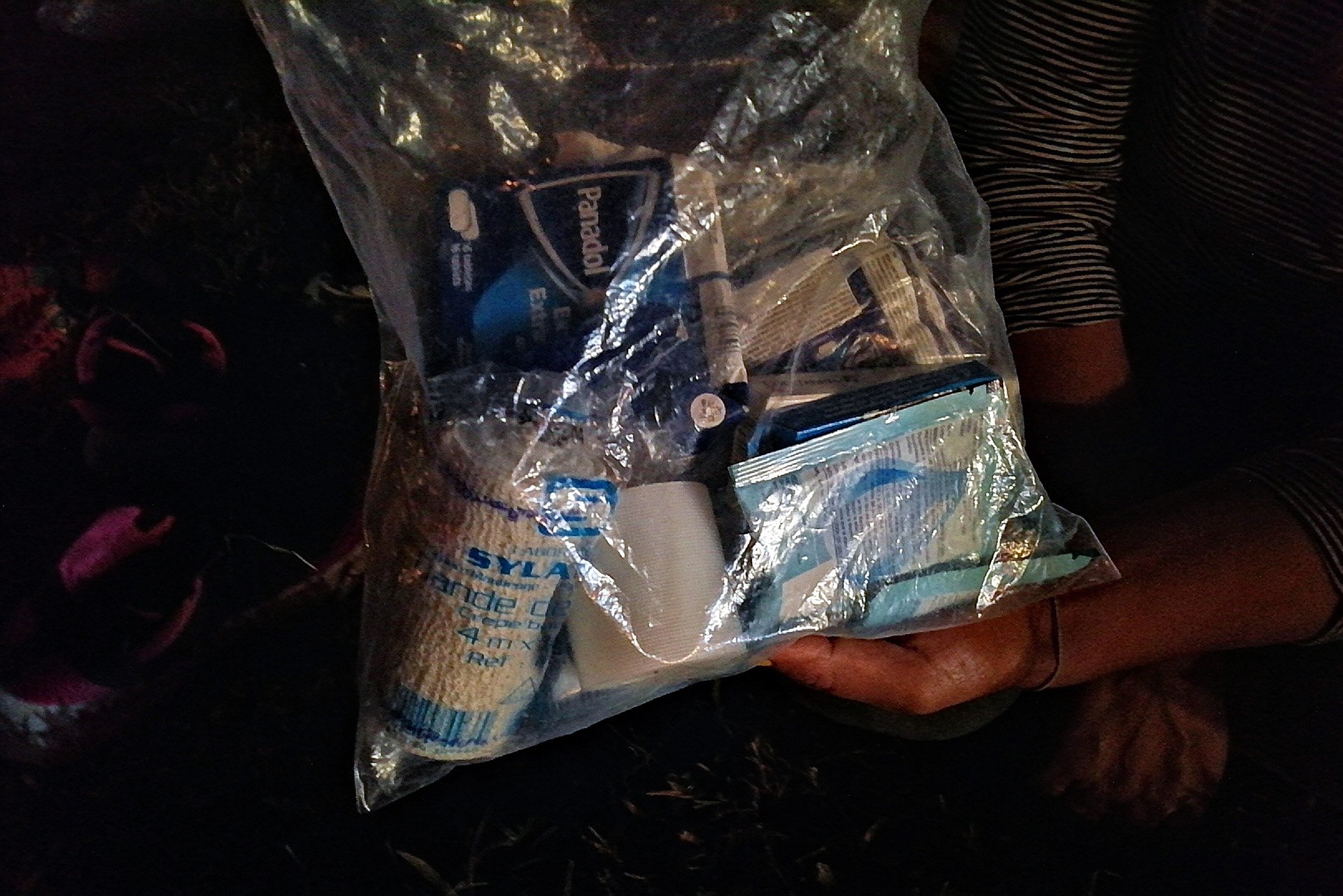 A pair of hands hold up a clear plastic bag full of medical supplies 